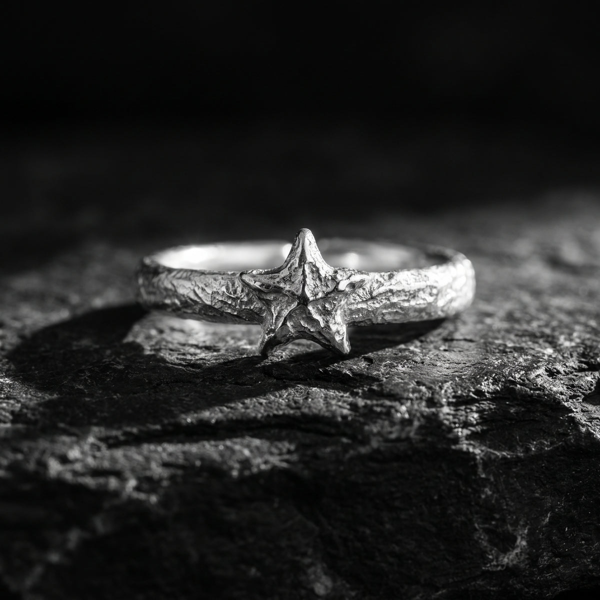 Close front view of a textured silver star ring resting on a dark rock surface.