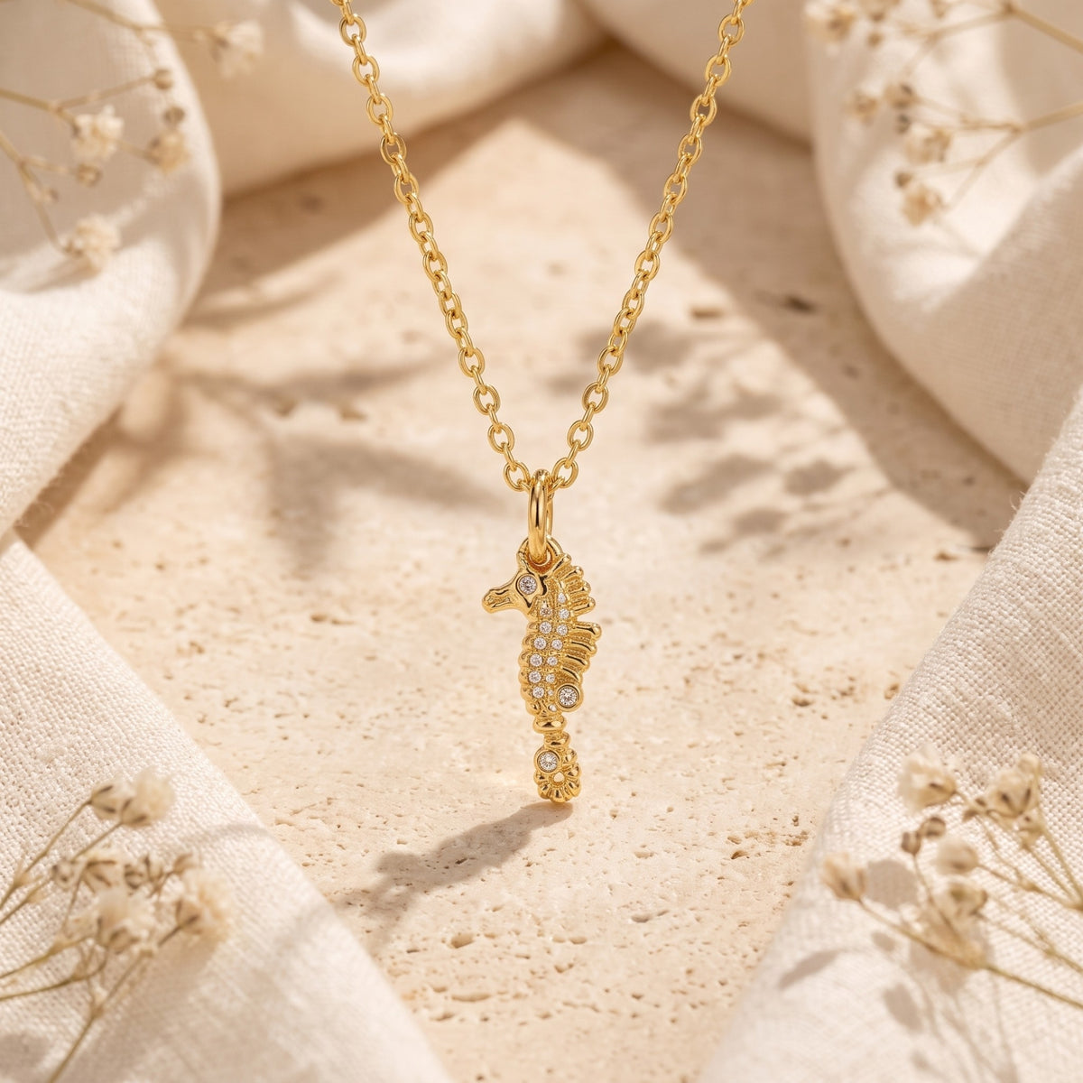 Gold-tone seahorse pendant with small clear crystals on a chain over a textured stone surface.