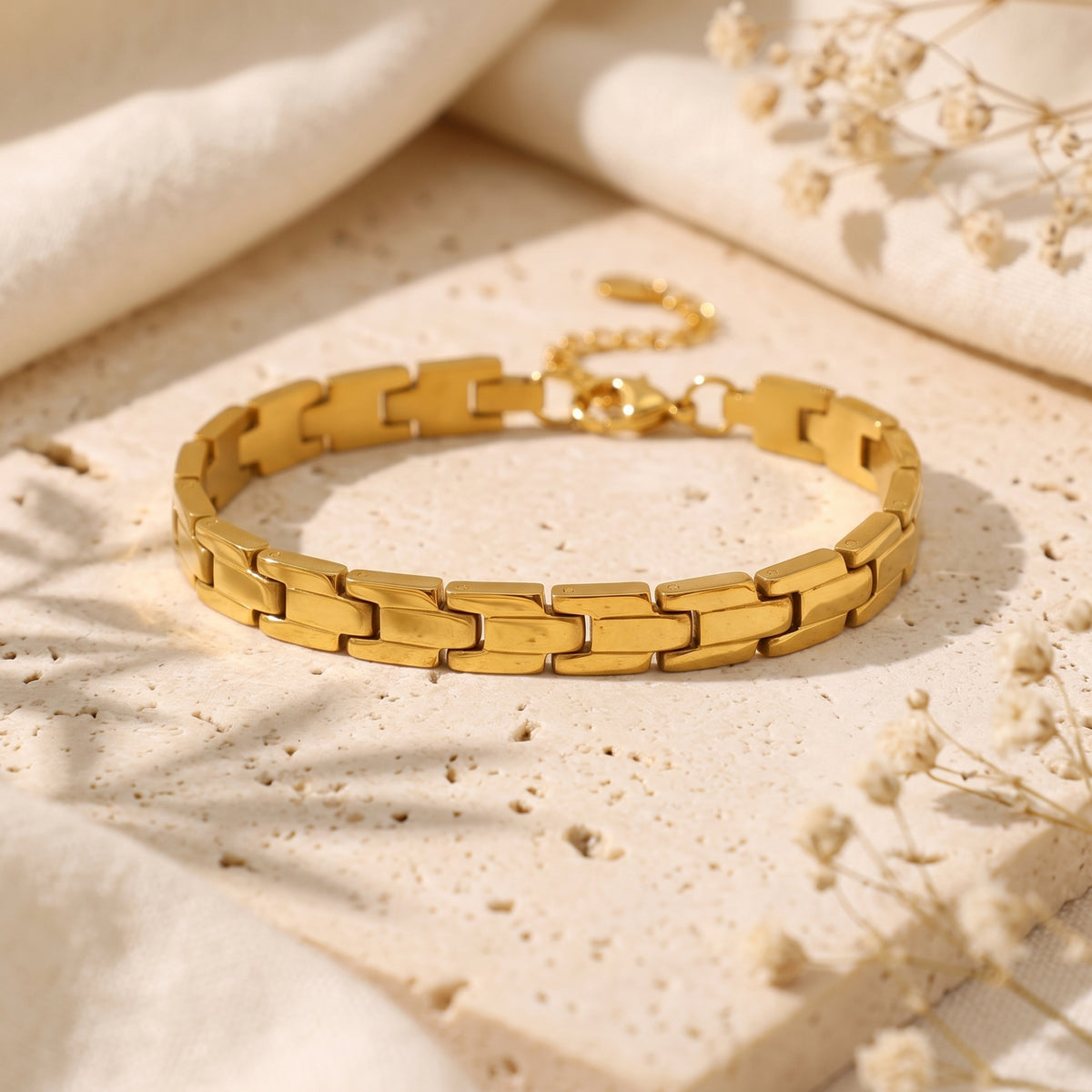 The gold-tone sculpted link bracelet resting on a textured travertine surface with soft shadows.