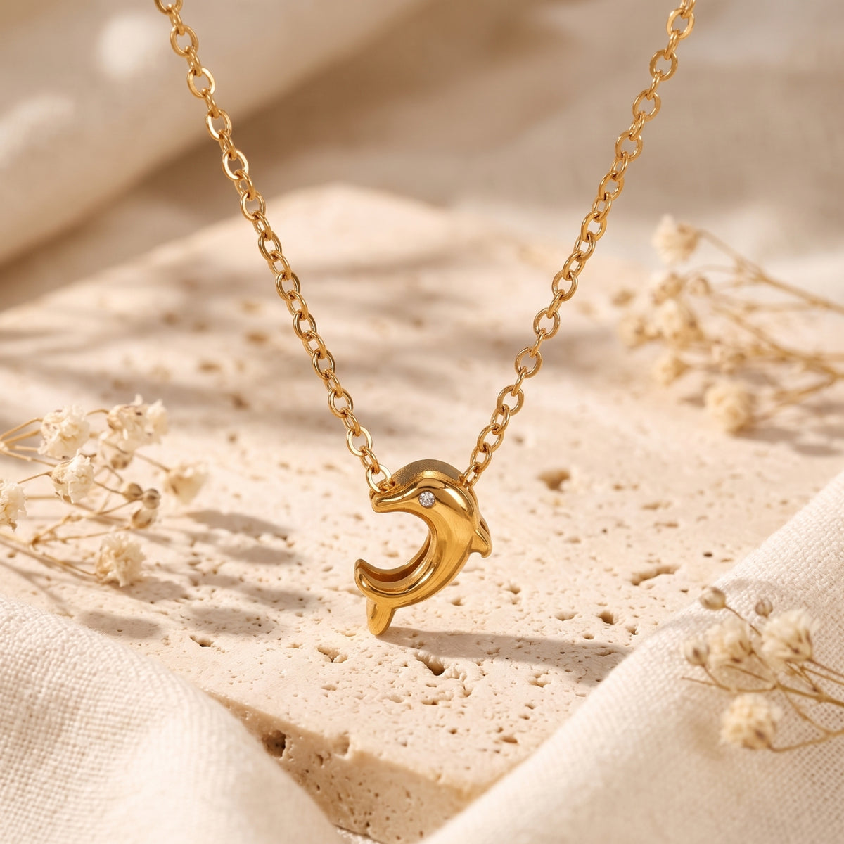 Close-up of a gold-tone dolphin pendant with a clear accent stone on an oval-link chain.