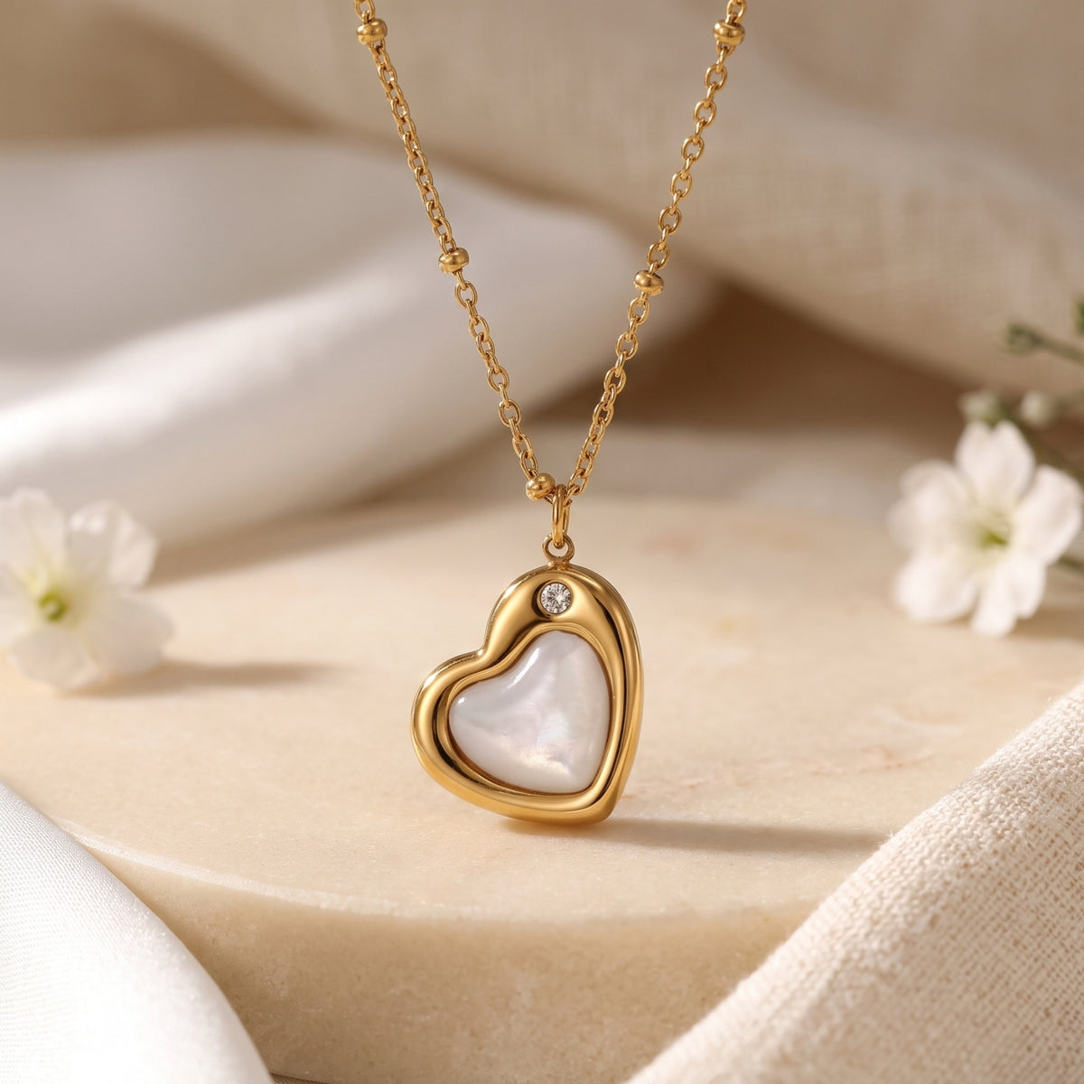 Close-up of a gold-tone heart pendant necklace with a pearl-like insert and crystal accent on a beaded chain.