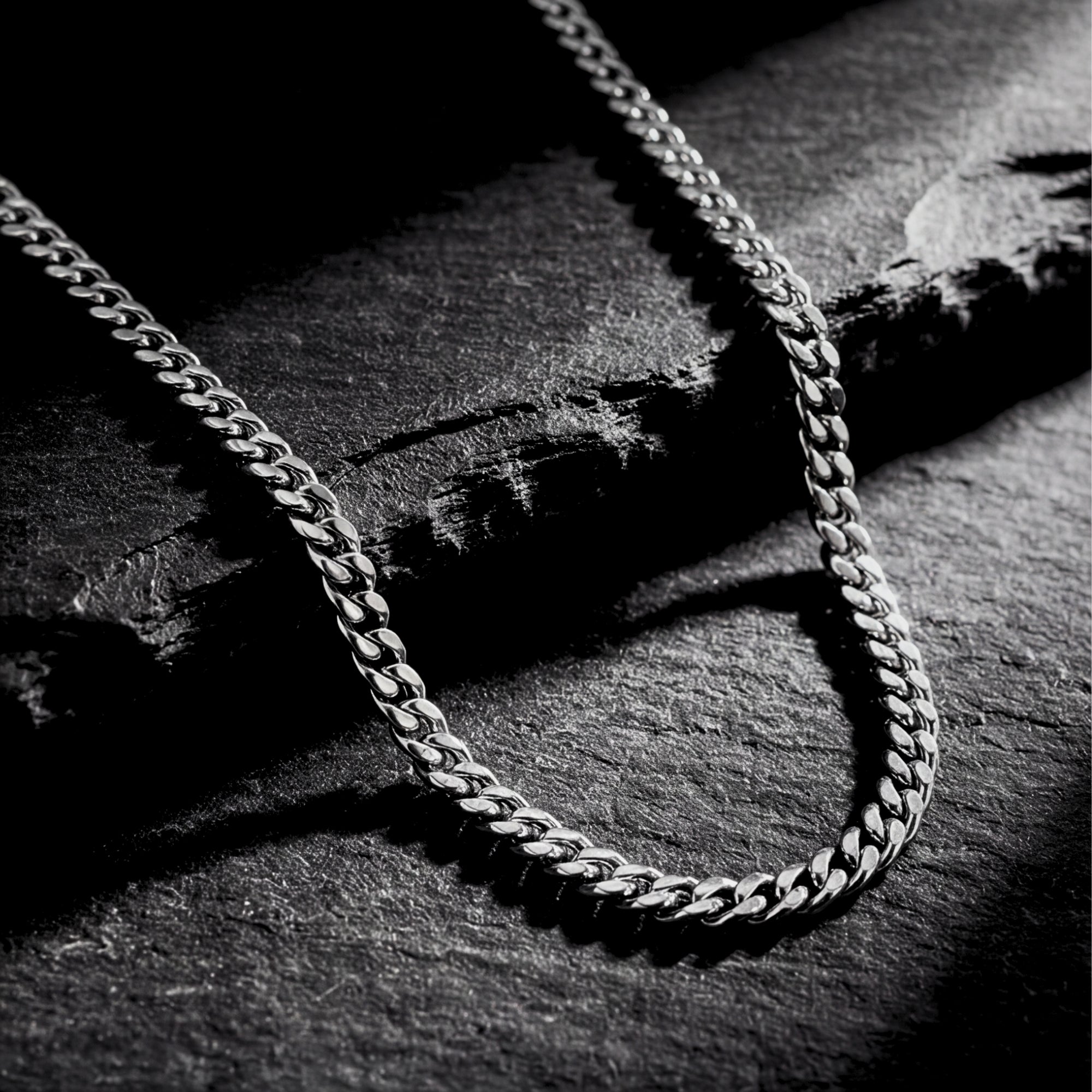 Silver 4mm Miami Cuban chain in 316L stainless steel draped over a dark textured stone surface.