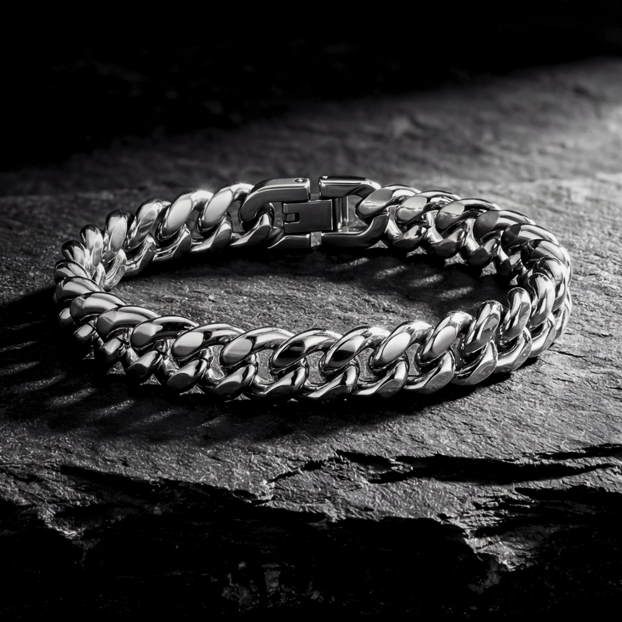 Silver stainless steel Cuban link bracelet for men displayed on a dark textured stone background.