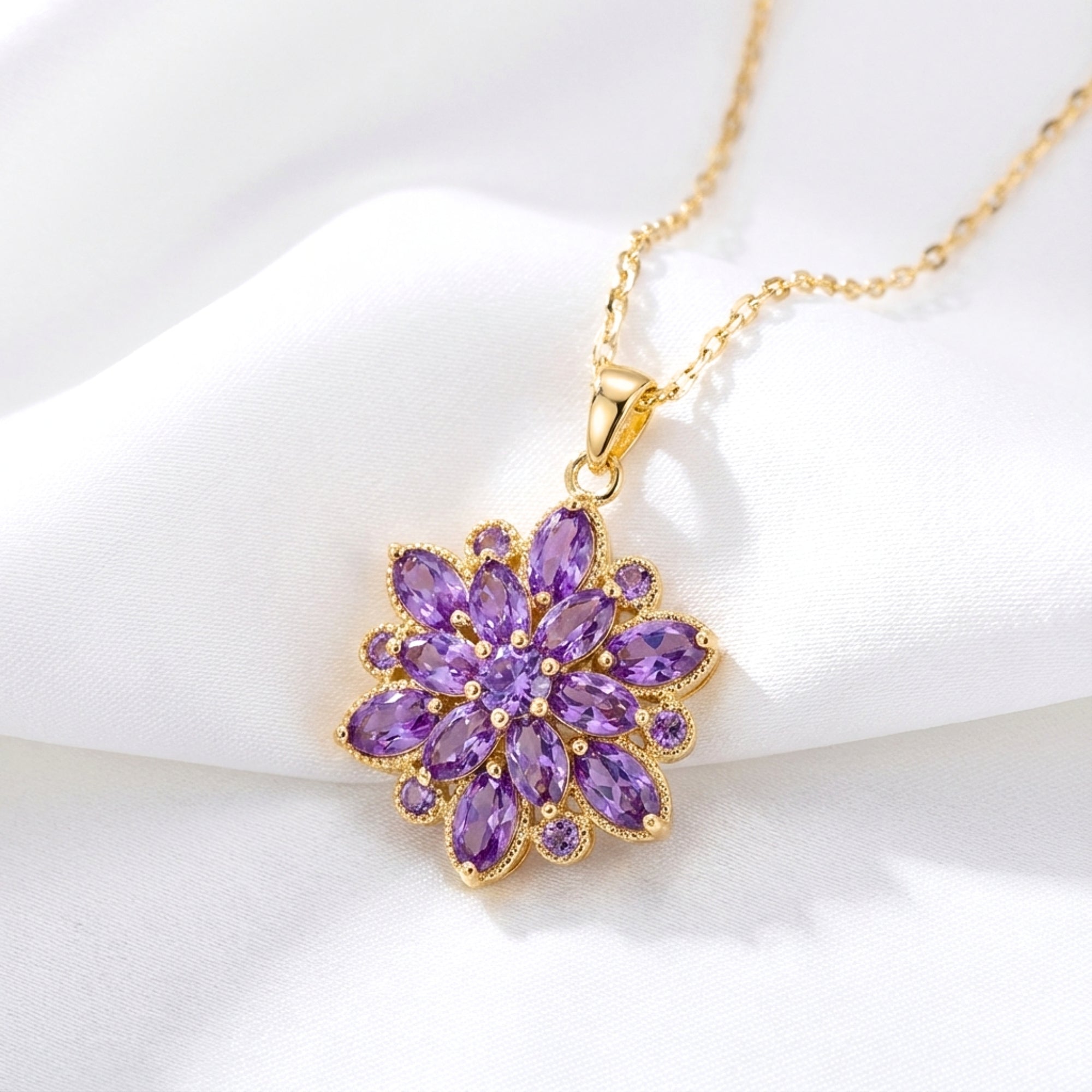 Gold-finished stainless steel Floriana pendant necklace with marquise-cut simulated amethyst on white fabric.