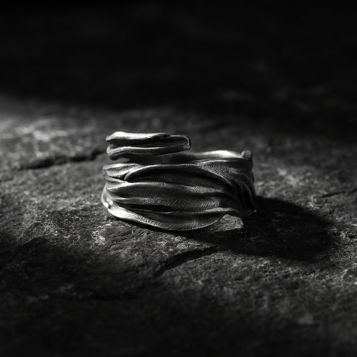 Textured silver open wrap ring with layered folds displayed on a dark rock surface.