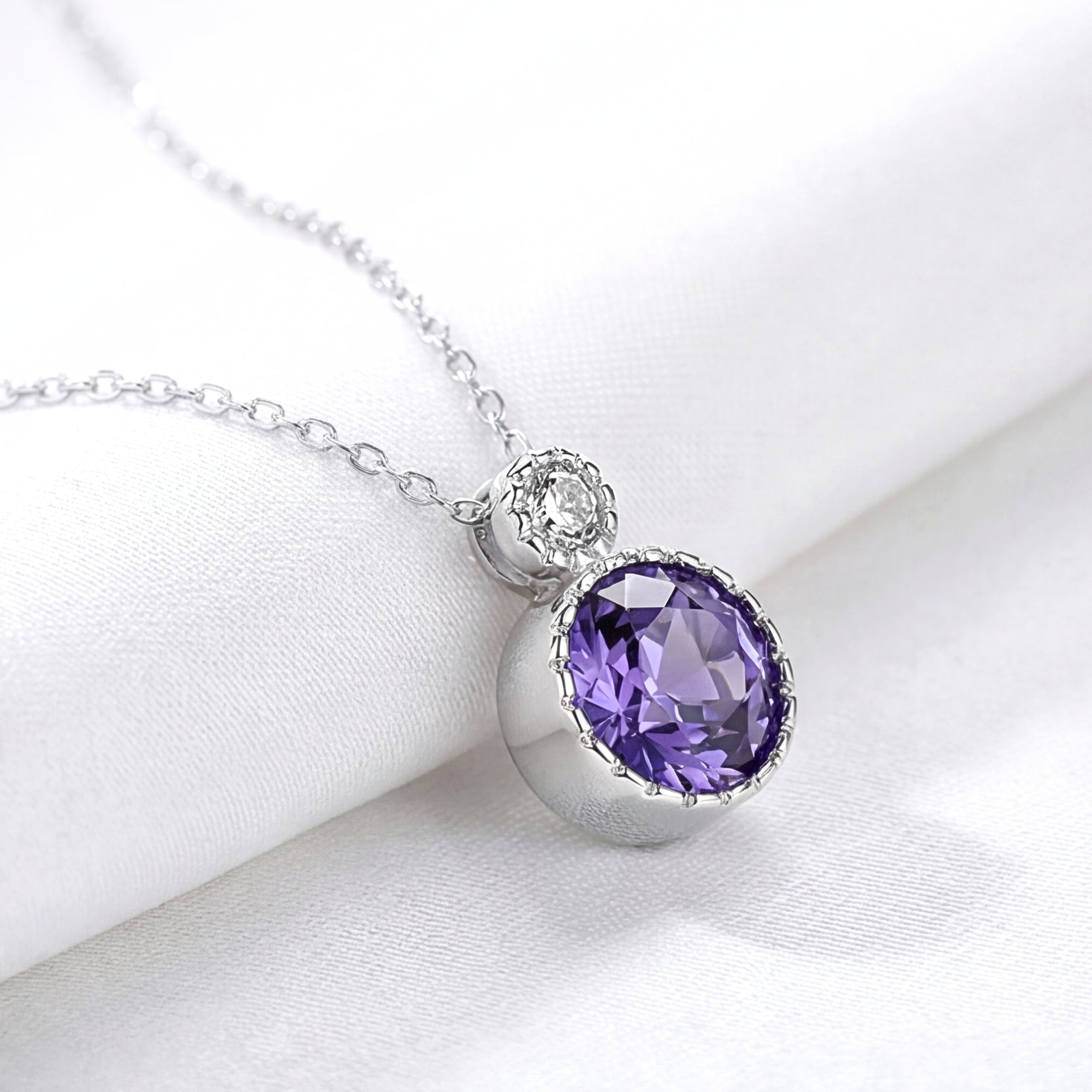 Round simulated amethyst drop necklace in S925 sterling silver, shown in a close-up on white fabric.