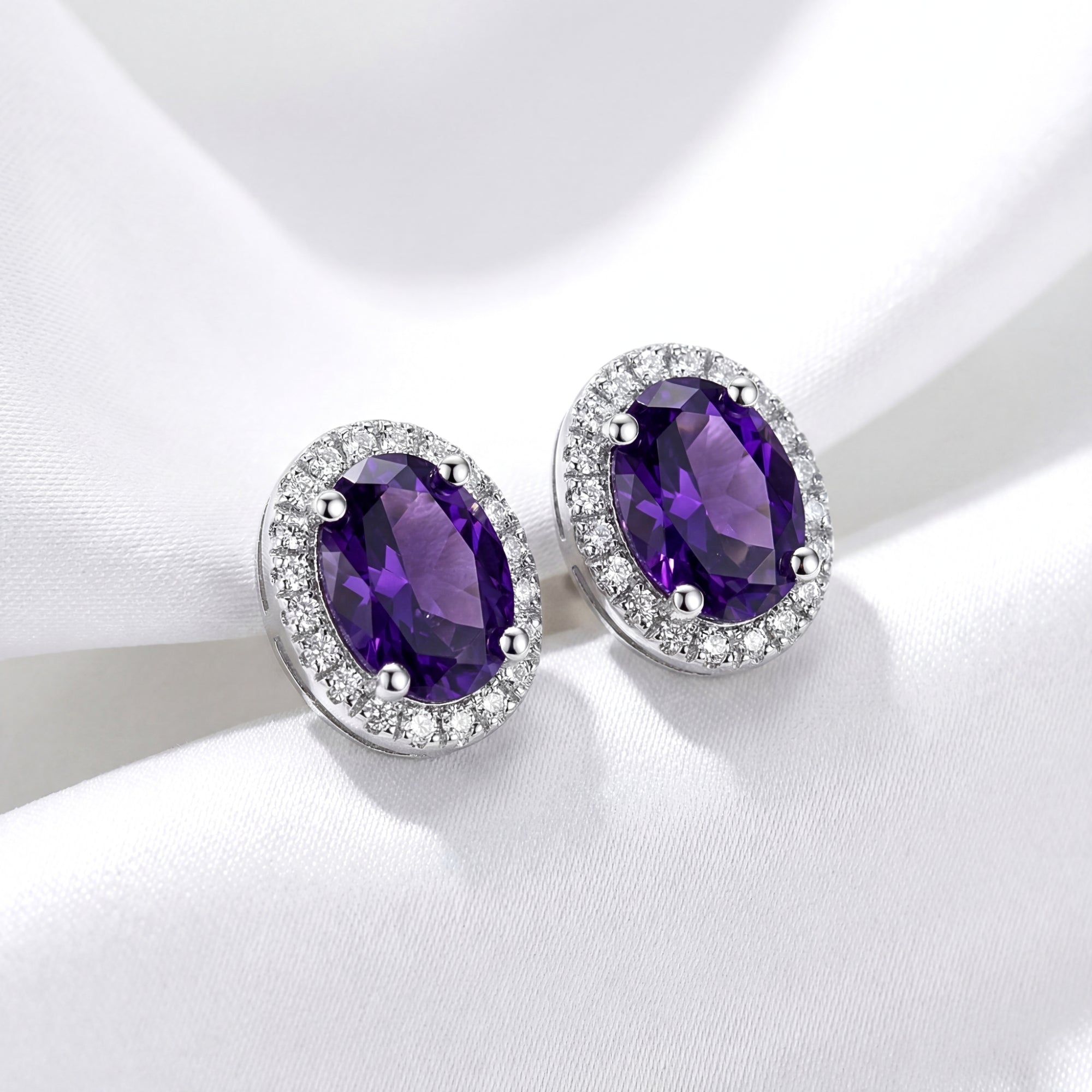 Oval simulated amethyst halo stud earrings in S925 sterling silver on a white draped fabric background.