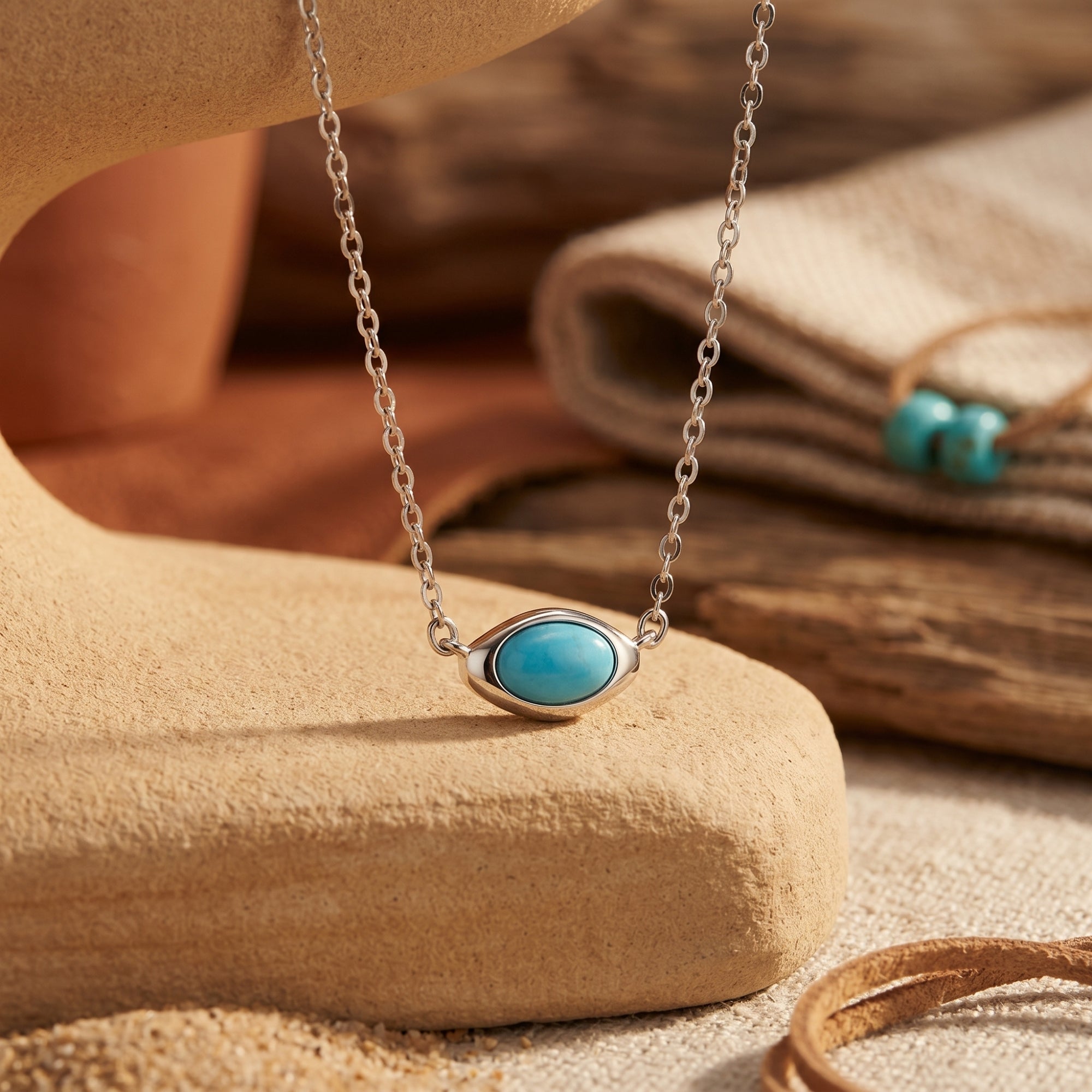 Silver turquoise necklace with a horizontal cabochon pendant displayed on a desert-themed stone background.