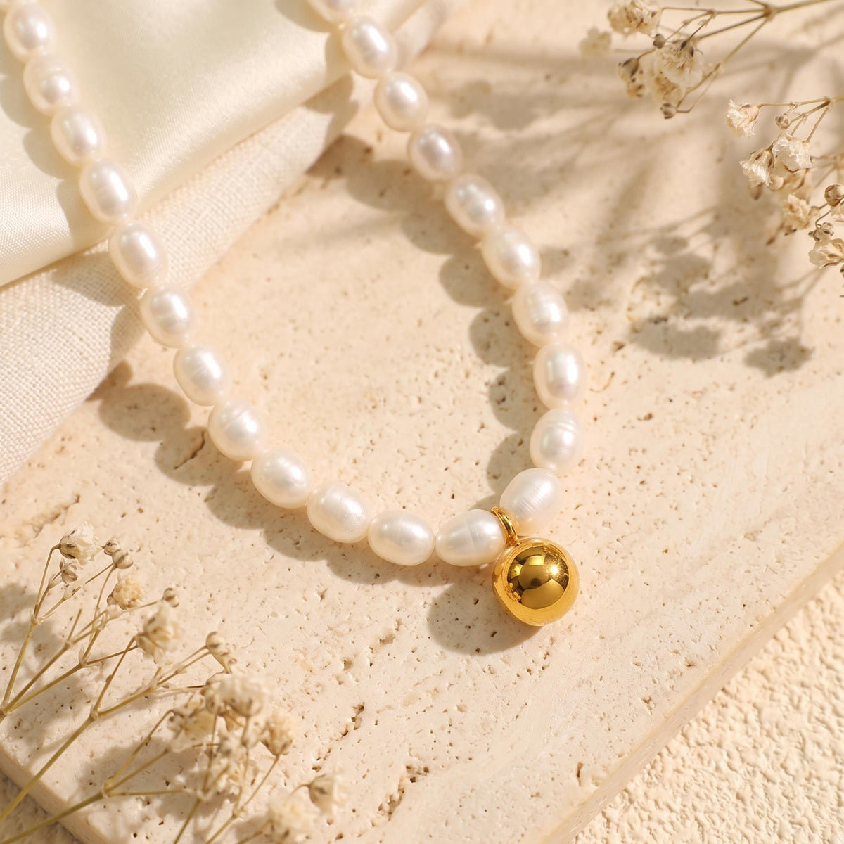 Close-up of white baroque pearl strand with a smooth gold-tone sphere pendant on a textured stone surface.