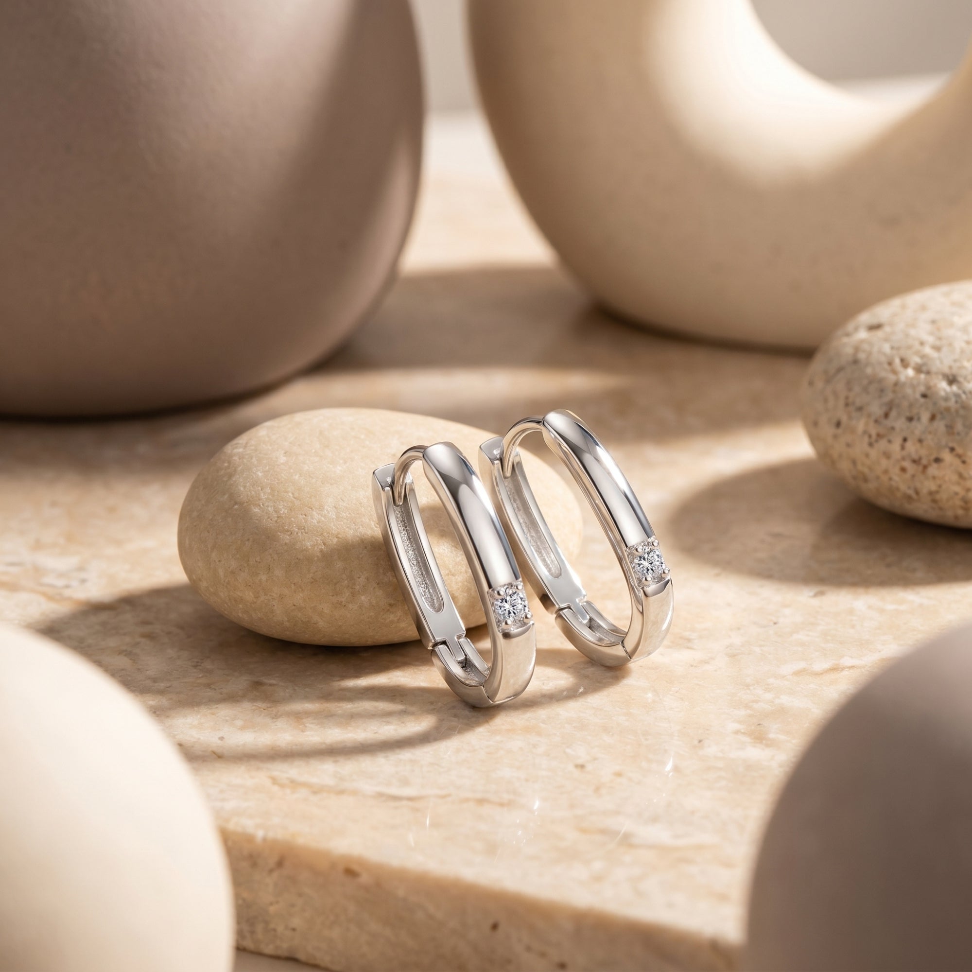 Fiorelle white gold huggie hoop earrings with round lab moissanite stones on a neutral stone lifestyle background.
