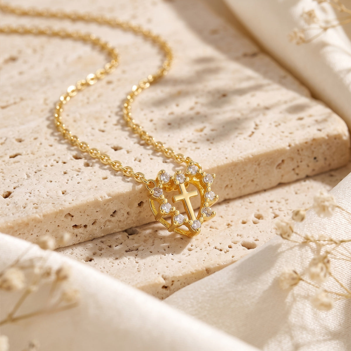 Close-up of the gold-tone heart halo cross pendant with clear cubic zirconia accents on a stone slab.