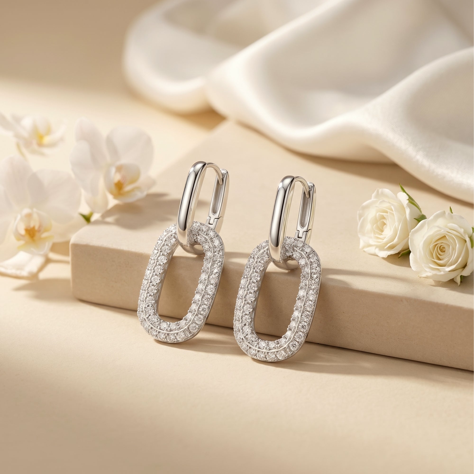 Silver moissanite double-link drop earrings on a neutral surface with white flowers.