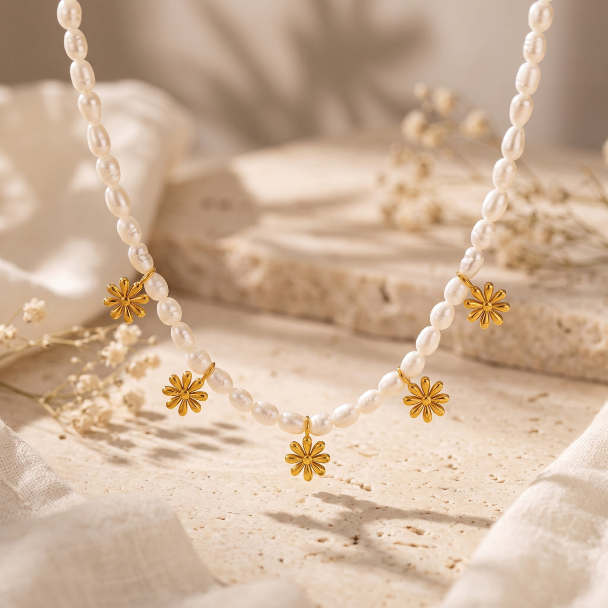 Close-up of a white pearl bead necklace with five gold-tone daisy charms displayed above textured stone.