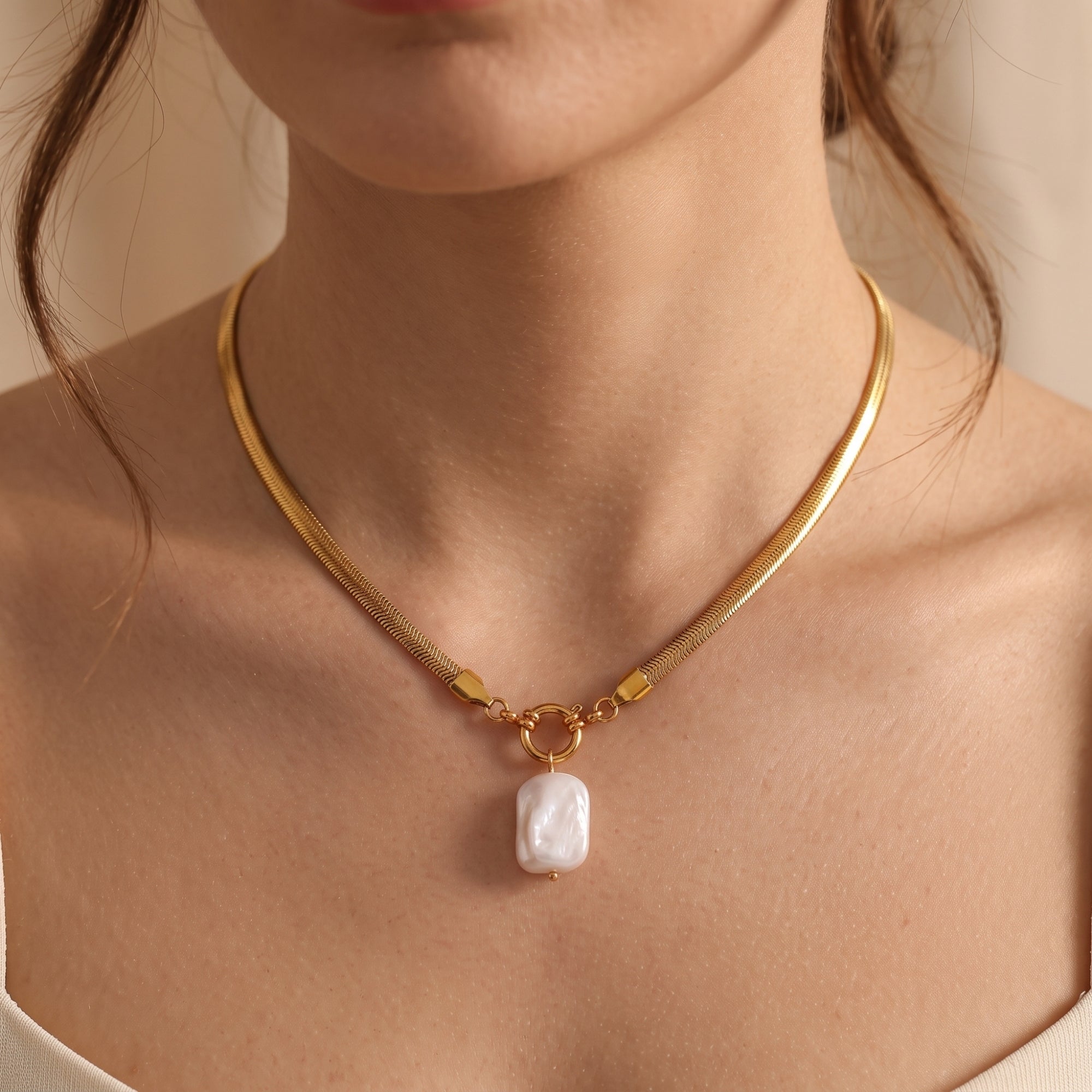 Front view of a woman wearing the gold herringbone snake chain necklace with a white baroque pearl pendant.