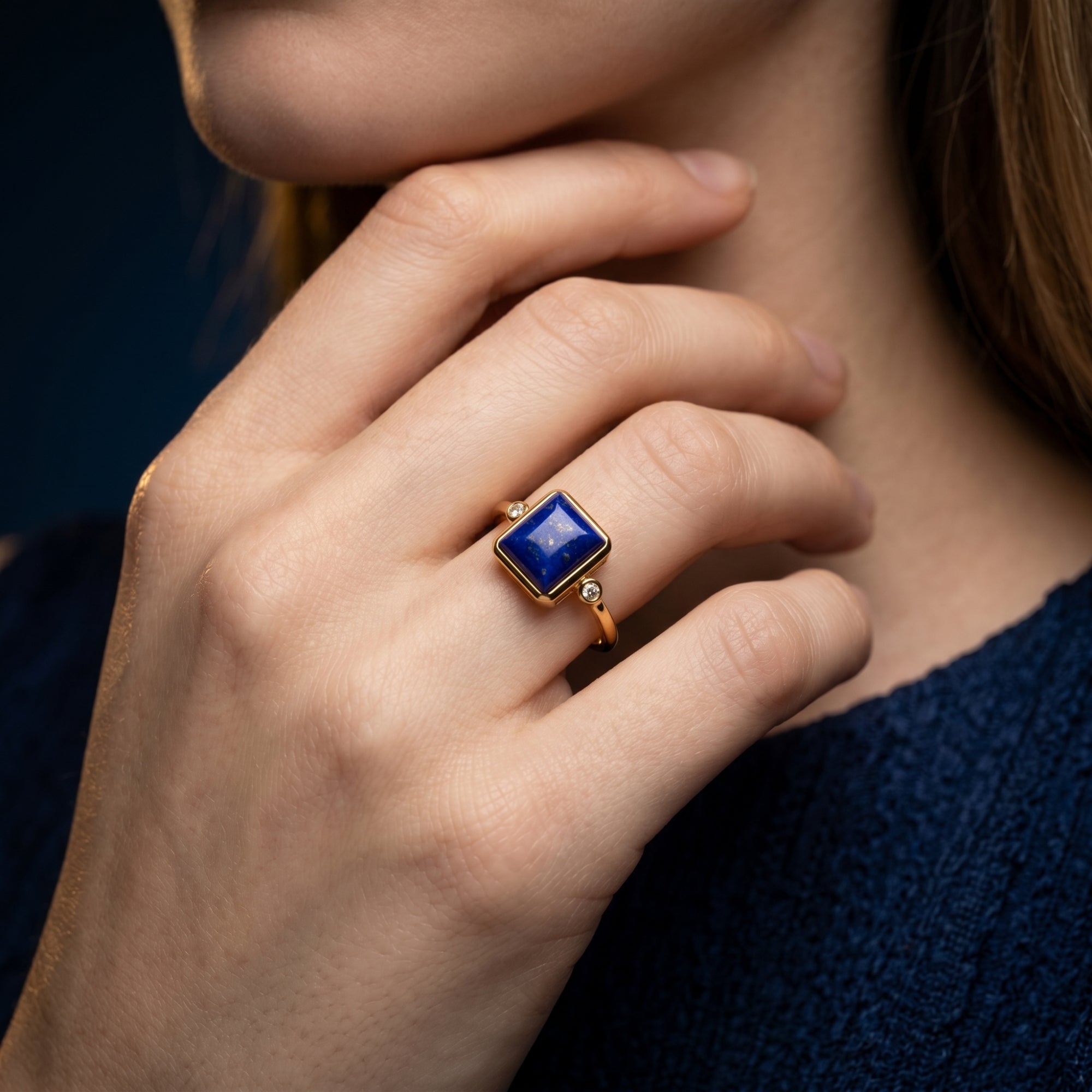 Woman wearing a yellow gold ring with a rectangular natural lapis lazuli stone on her finger.