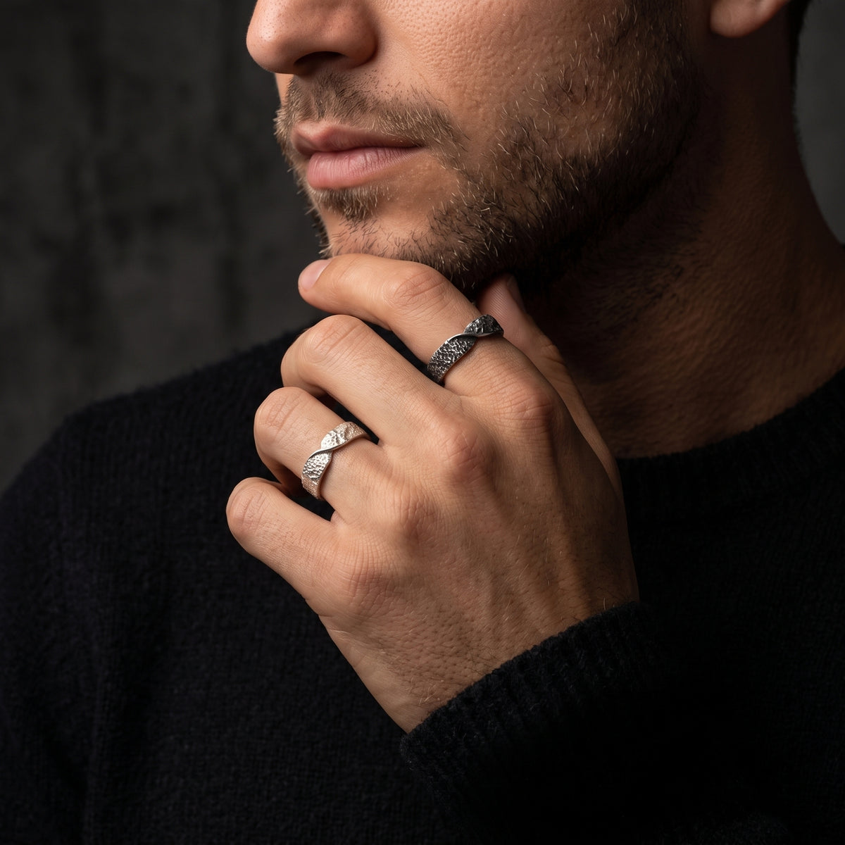 Man wearing natural silver and dark oxidized hammered twist rings on separate fingers, hand near chin.