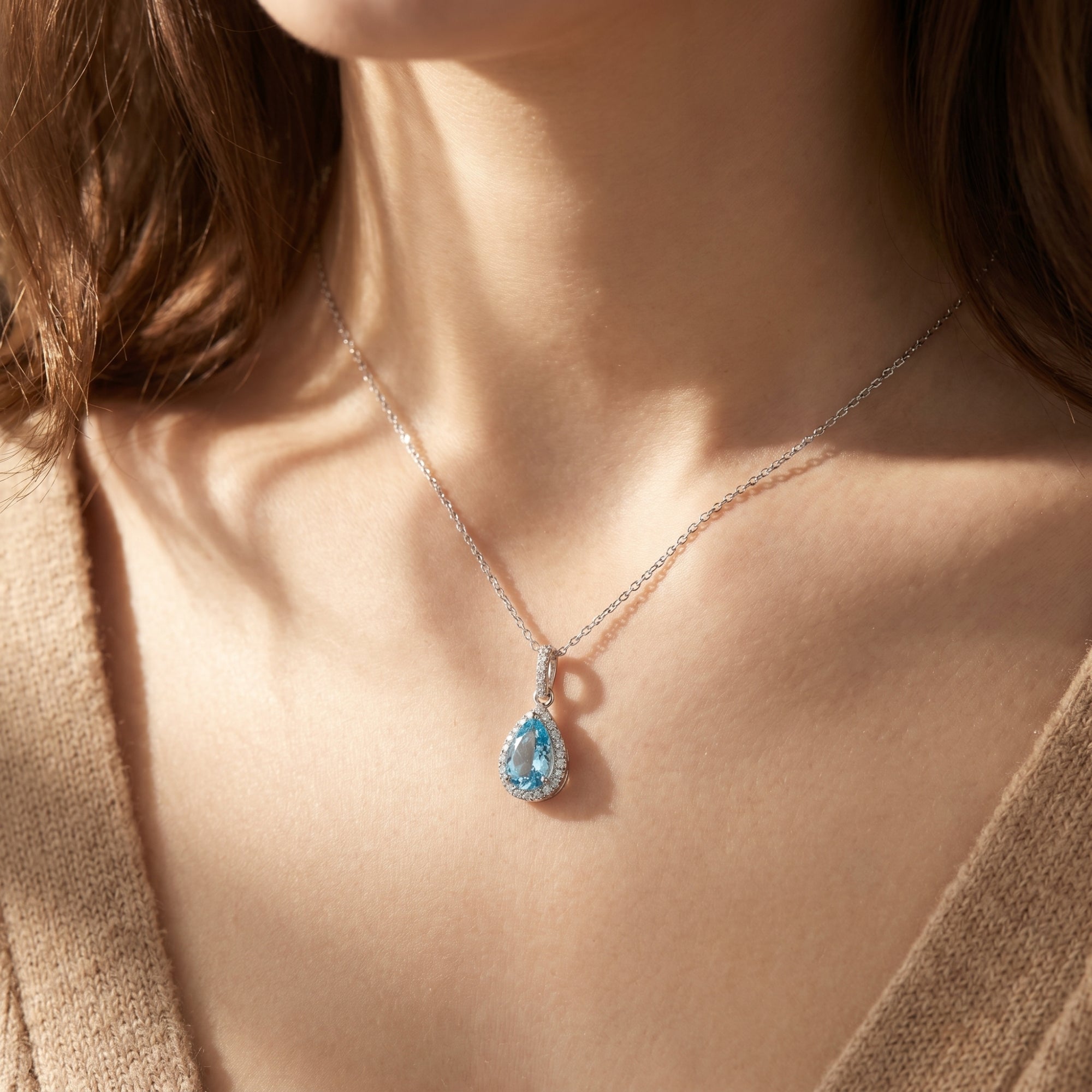 Woman wearing the pear-shaped aquamarine halo necklace in sterling silver.
