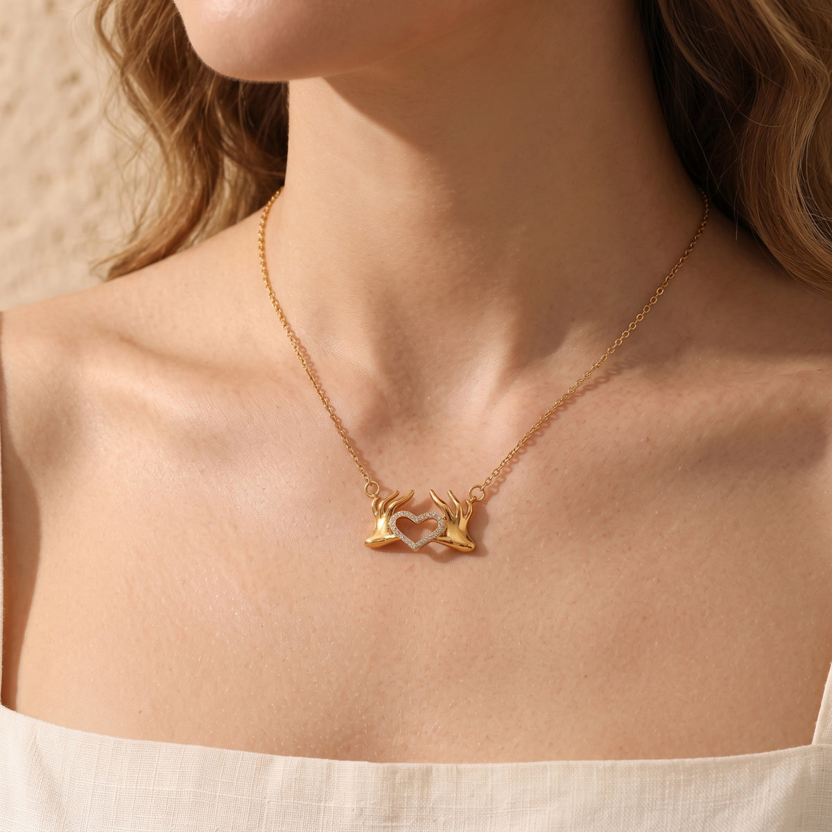 Model wearing the gold-tone heart hands pendant necklace centered at the collarbone over a white top.