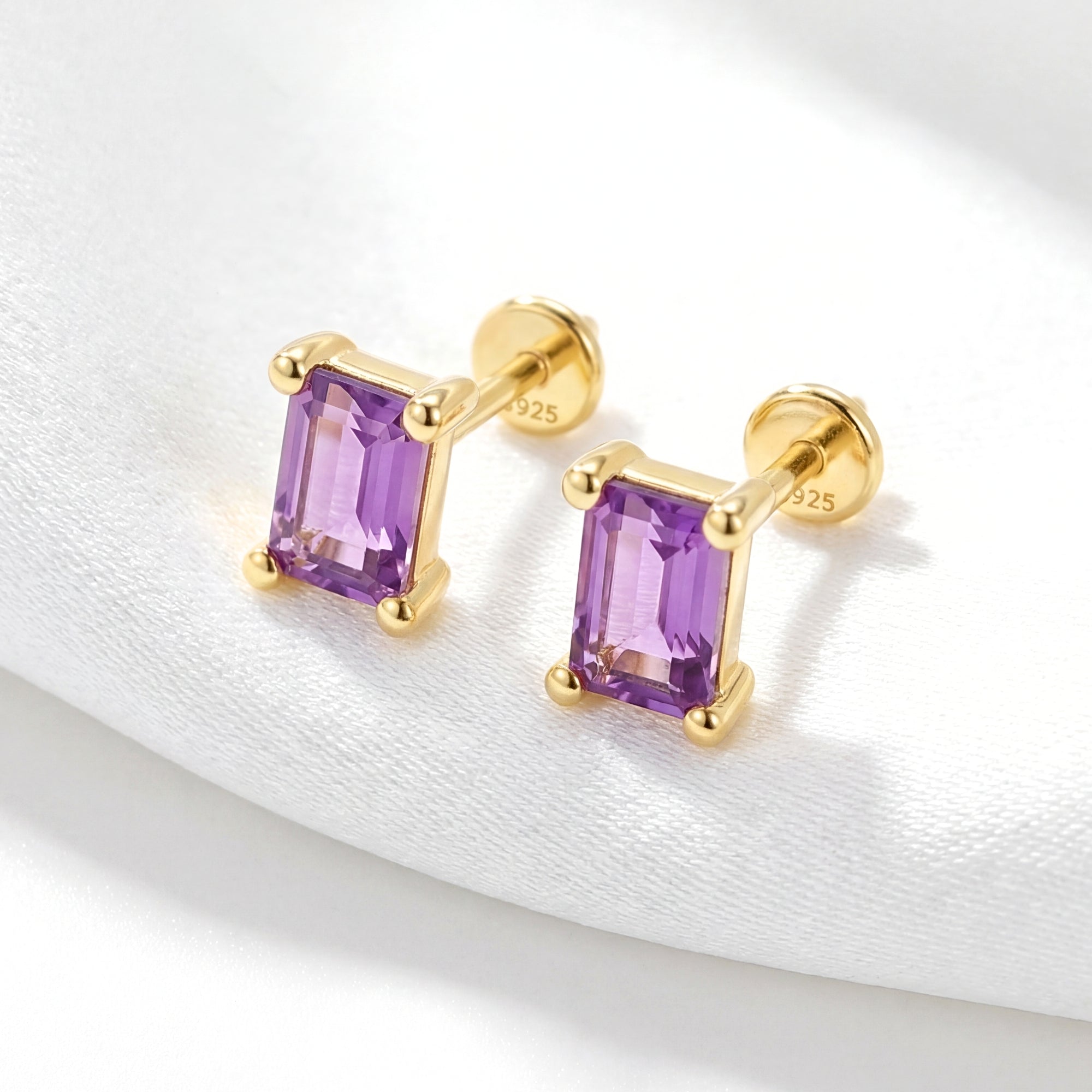 Angled view of 18K gold vermeil emerald cut amethyst studs showing the four-prong setting on white fabric.