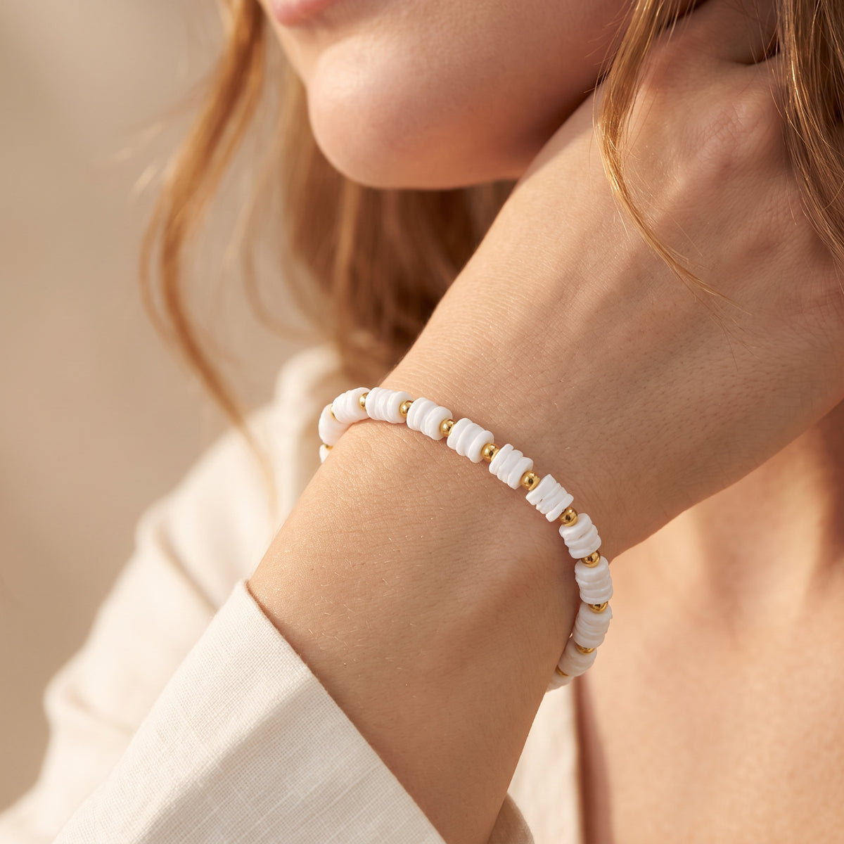 Close-up of the white disc-bead bracelet with gold-tone spacers worn on a wrist.
