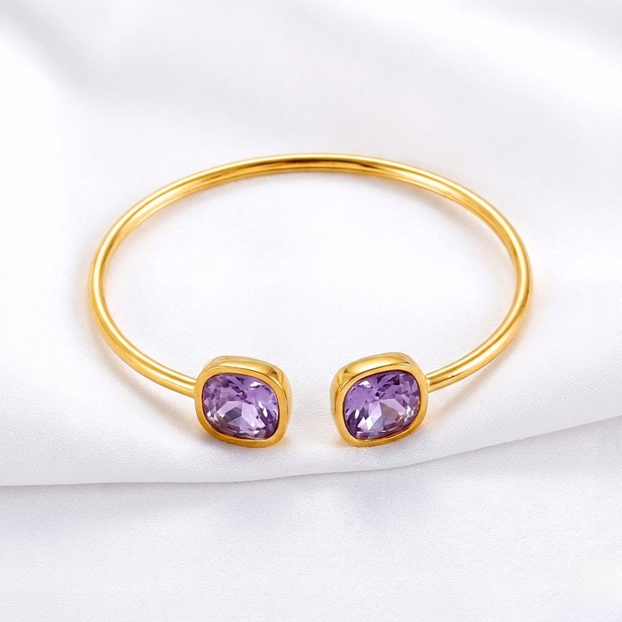 Front view of the gold Aurelia bangle with two cushion-cut simulated amethyst stones on white fabric.