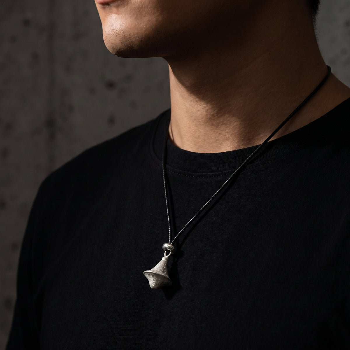 Close-up of a person wearing the textured silver double-cone pendant on a black cord over a black T-shirt.