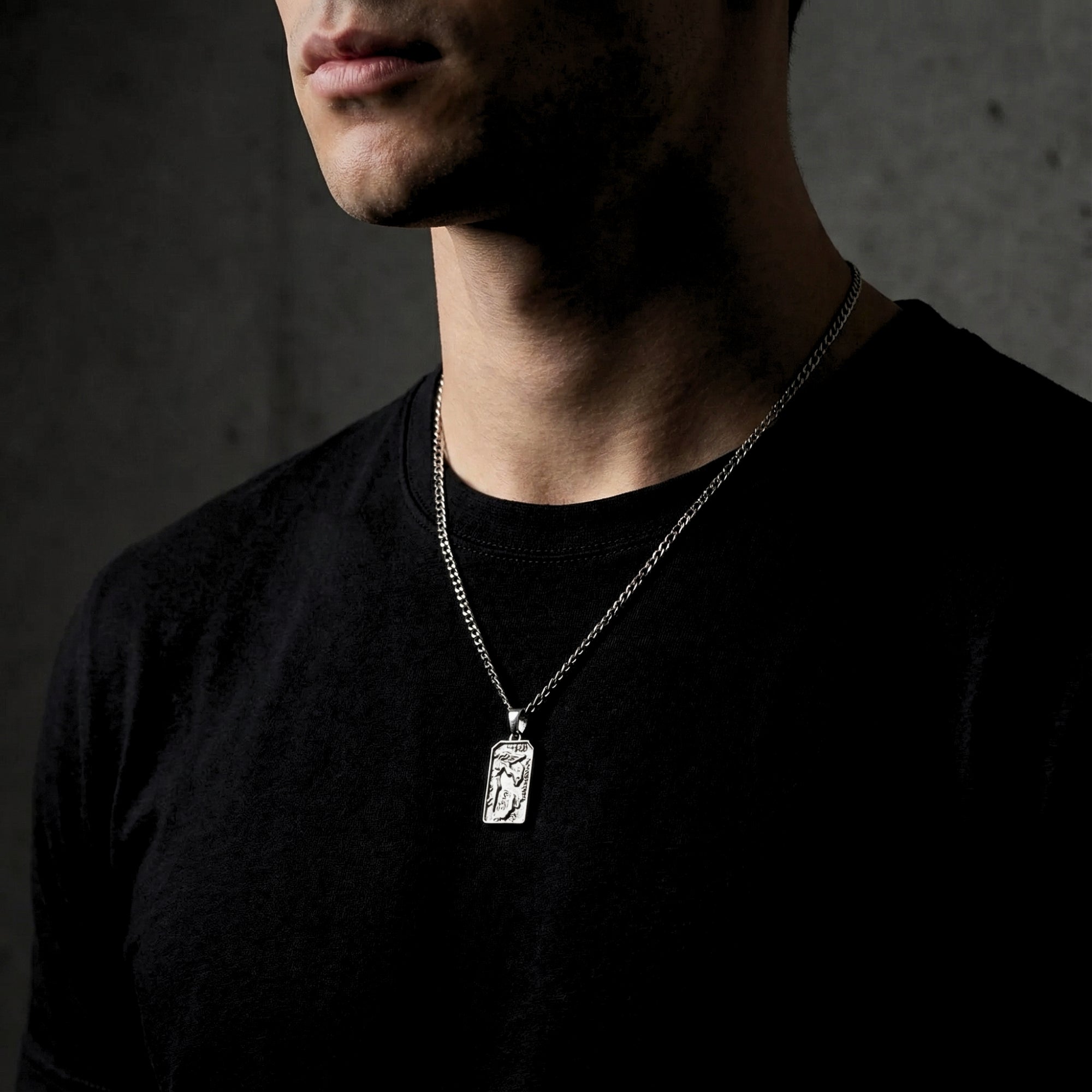 Men's silver stainless steel St. Michael's Victory pendant necklace worn by a model over a black t-shirt.