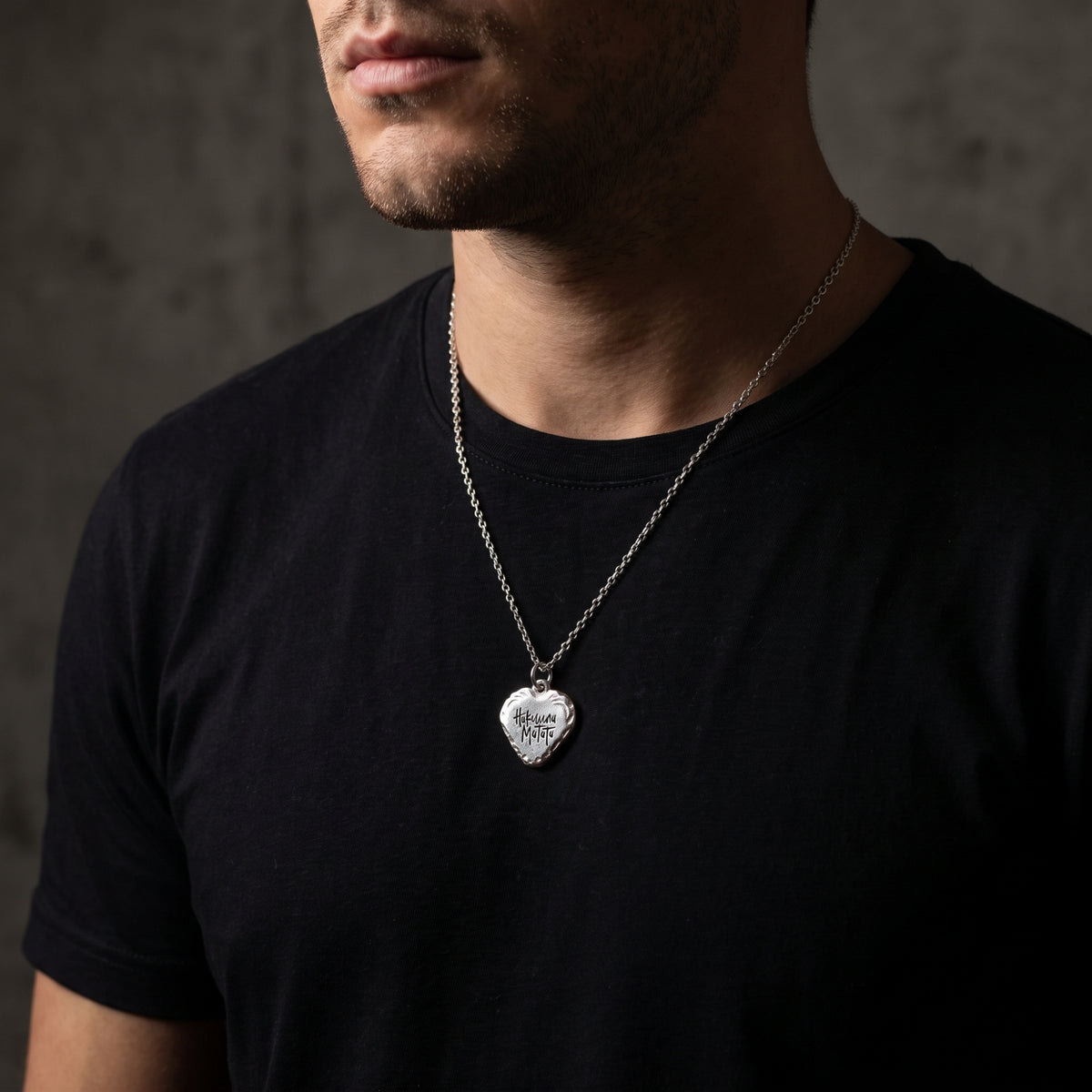 Front view of a man wearing the silver Hakuna Matata heart pendant necklace over a black T-shirt.
