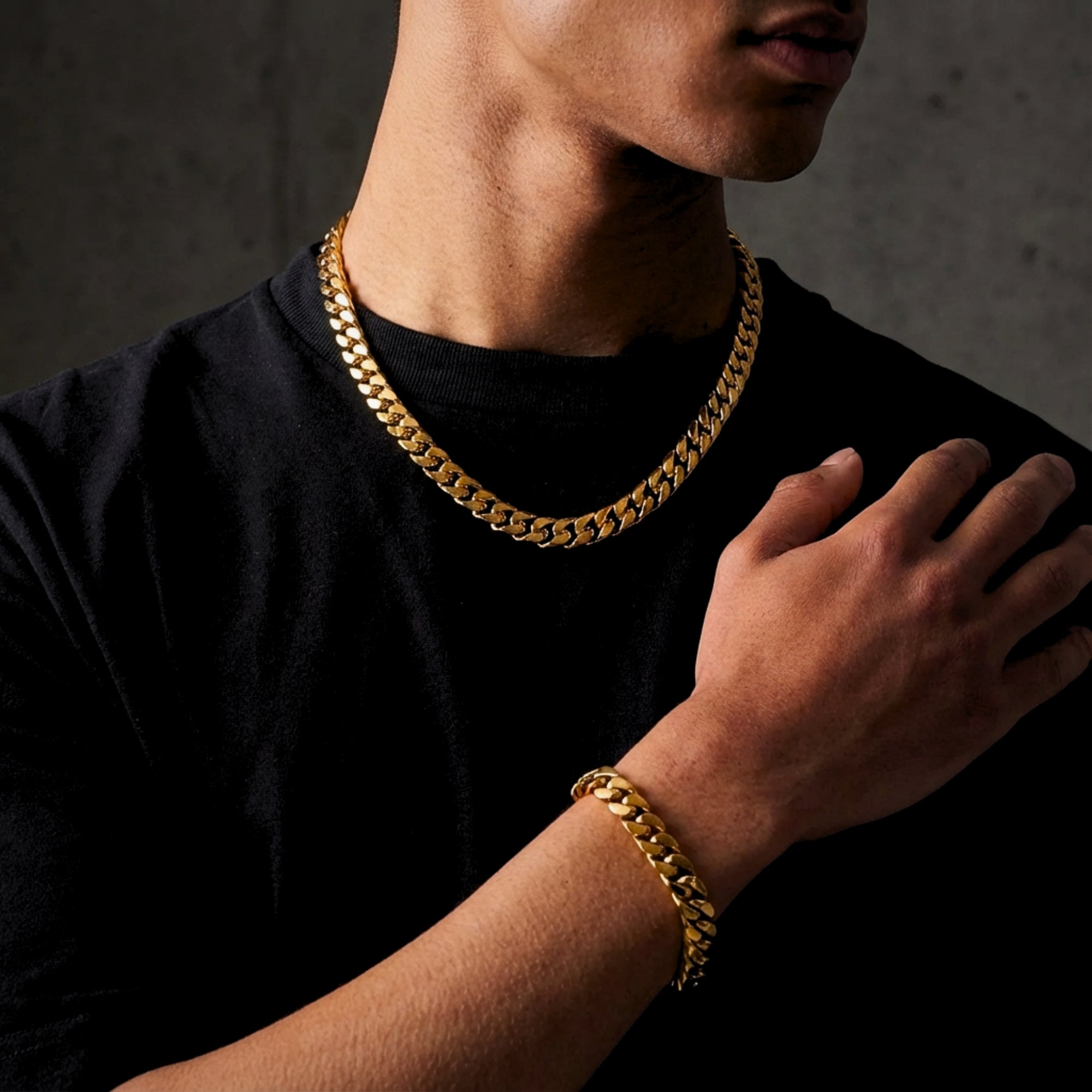 Man wearing a gold-tone stainless steel Cuban link chain and matching bracelet over a black t-shirt.