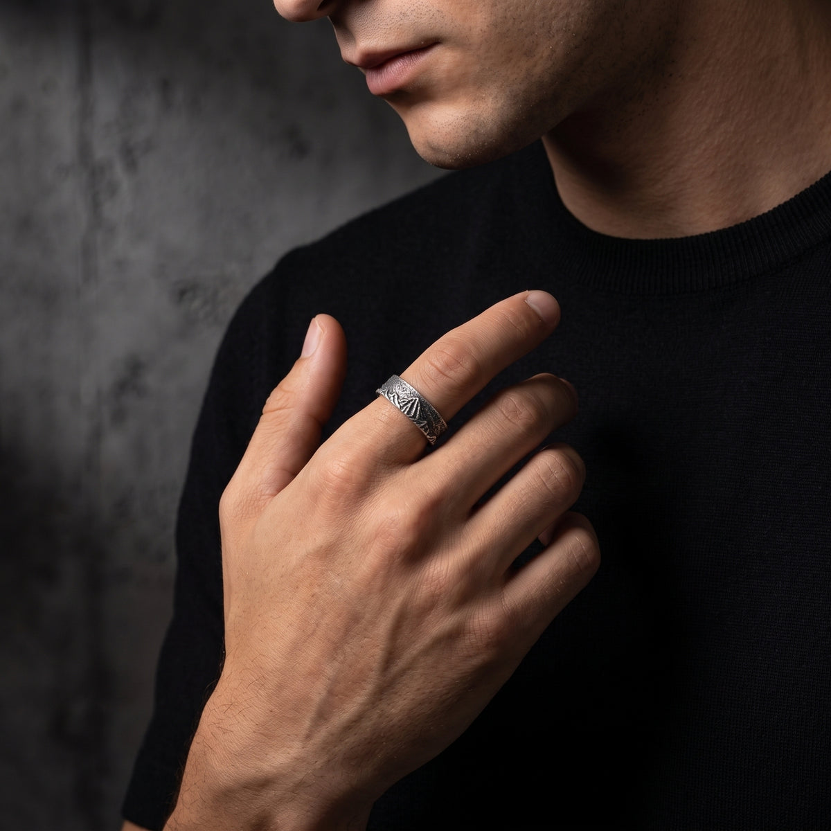 Man wearing the silver carved mountain ring on his index finger against a black sweater.