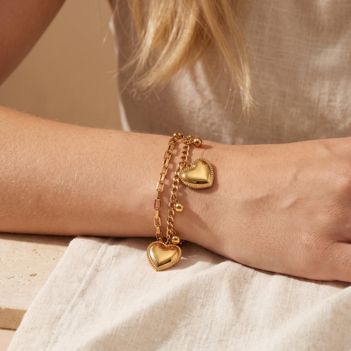 Close-up of the gold-tone double-chain bracelet worn on a wrist, with heart charms and dangling bead drops.