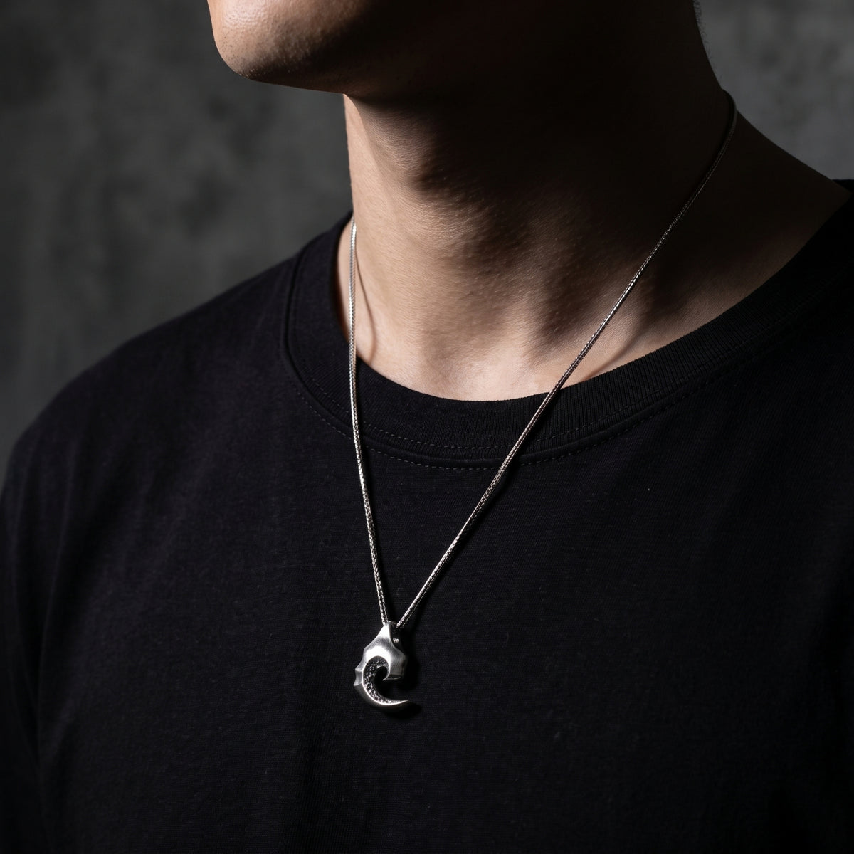 Silver wave scroll pendant necklace worn over a black t-shirt on a model.