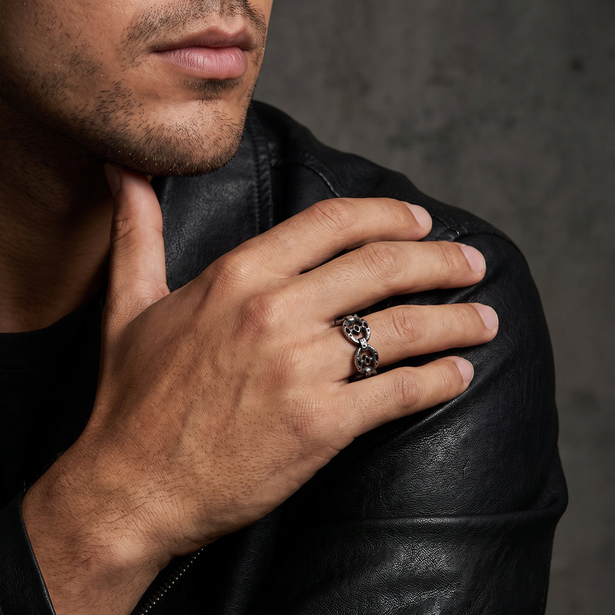 Man in a black leather jacket resting his hand near his chin while wearing the silver oval-link ring.