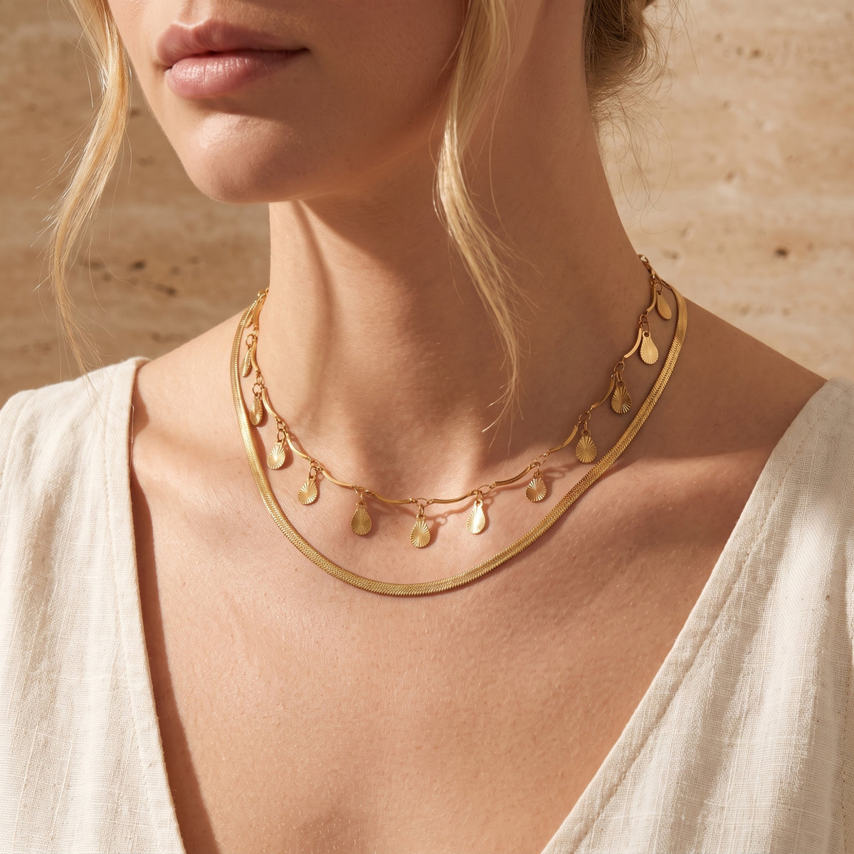 Model wearing the gold-toned layered necklace with a flat snake chain and dangling textured teardrops.
