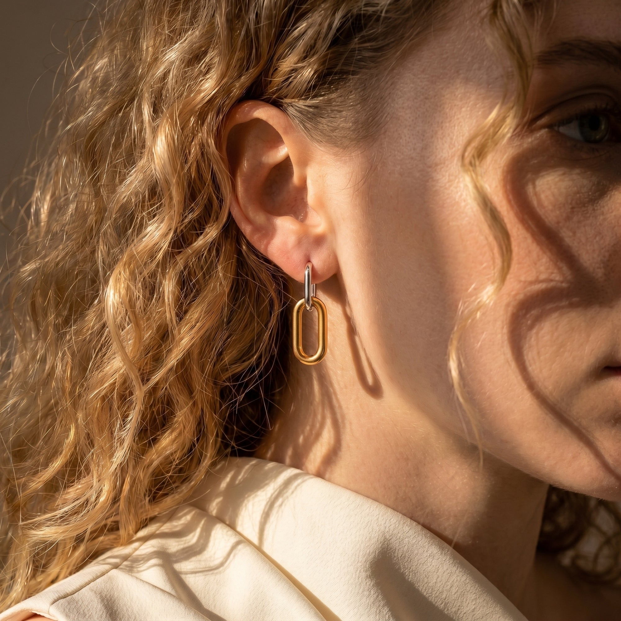 Two-tone silver and 18K gold plated link earrings worn on a model's ear.