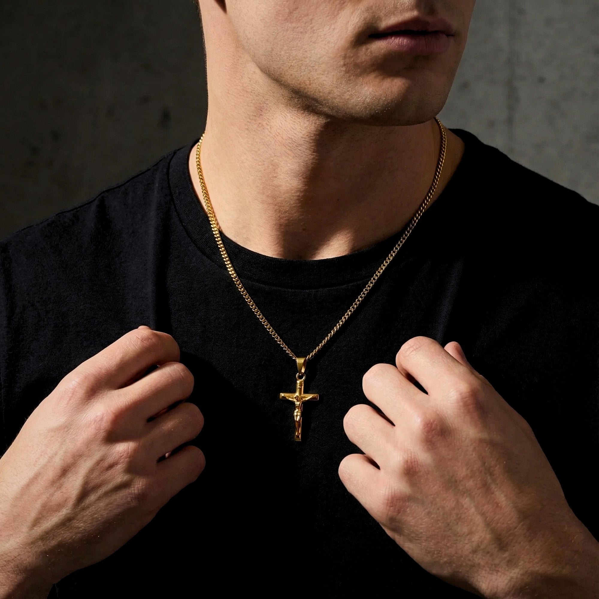 Man wearing the gold stainless steel Divine Cross crucifix pendant on a curb chain over a black t-shirt.