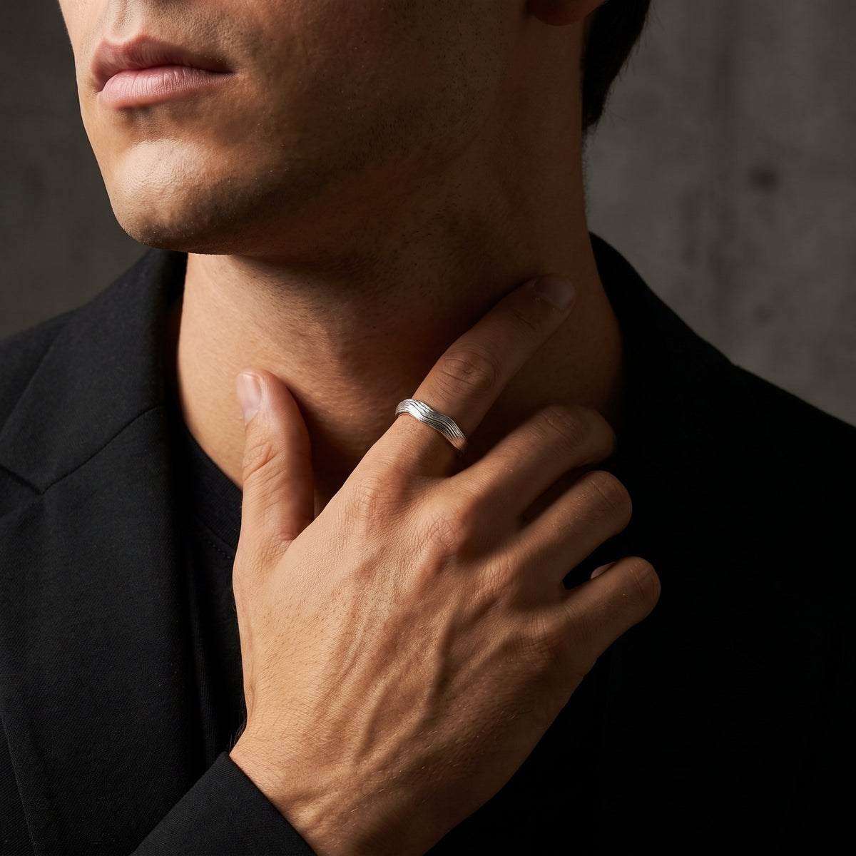 Man wearing the silver textured wave ring on his index finger while touching his neck.