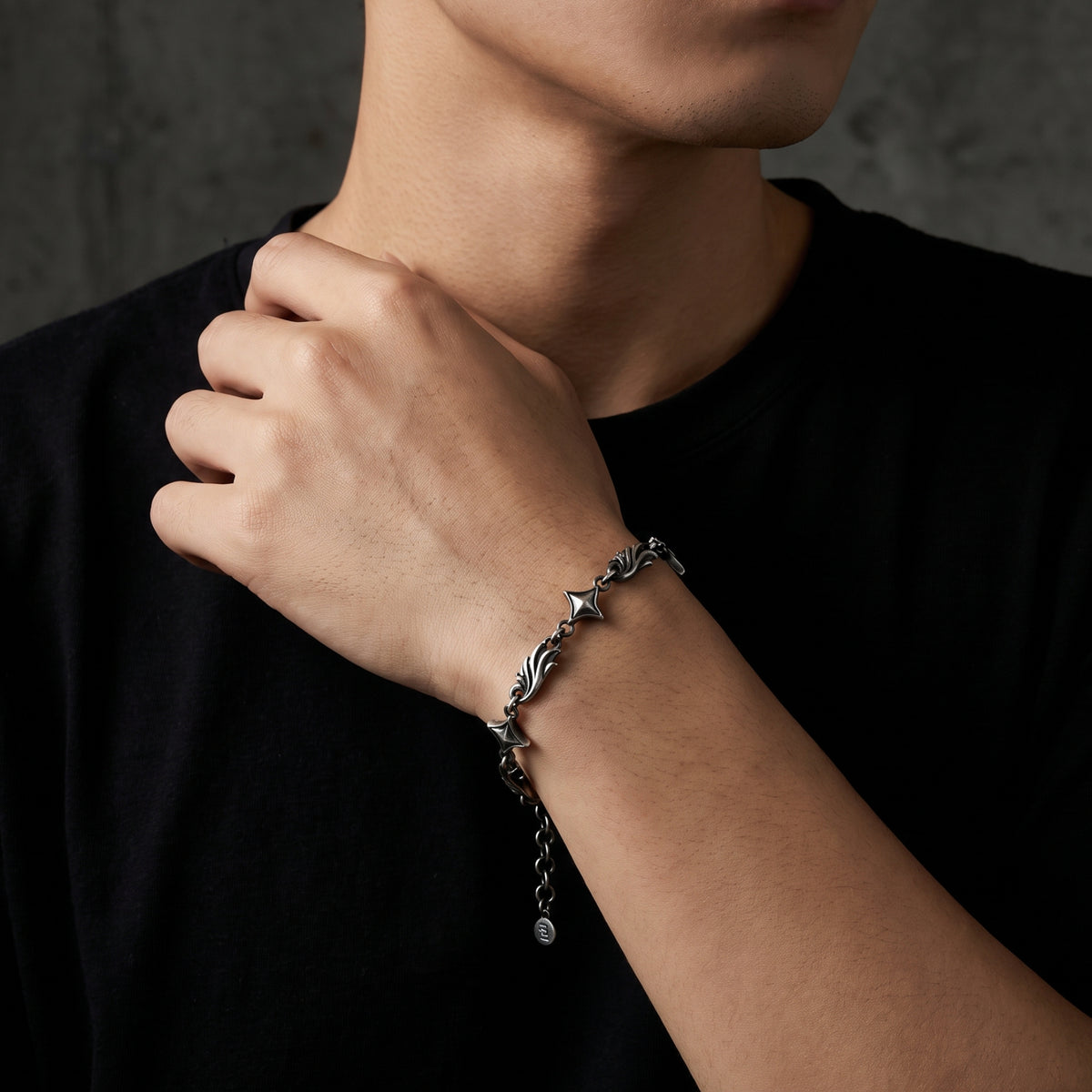 Model wearing the silver star link bracelet on his wrist with one hand raised near his neck.