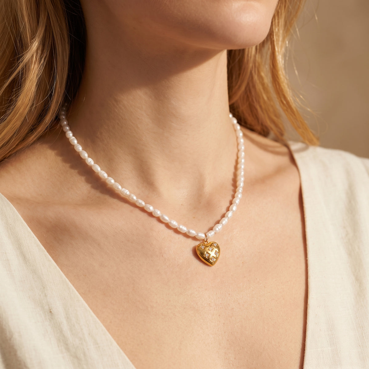 Front view of a model wearing the white pearl necklace and starburst-set gold-tone heart pendant.