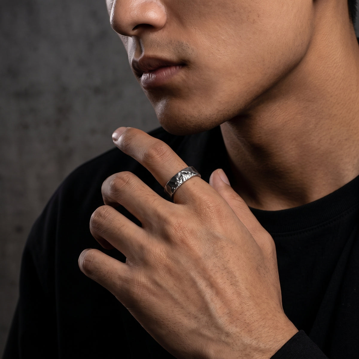 Close-up of a man touching his chin while wearing the textured silver ring with a carved mountain ridge.