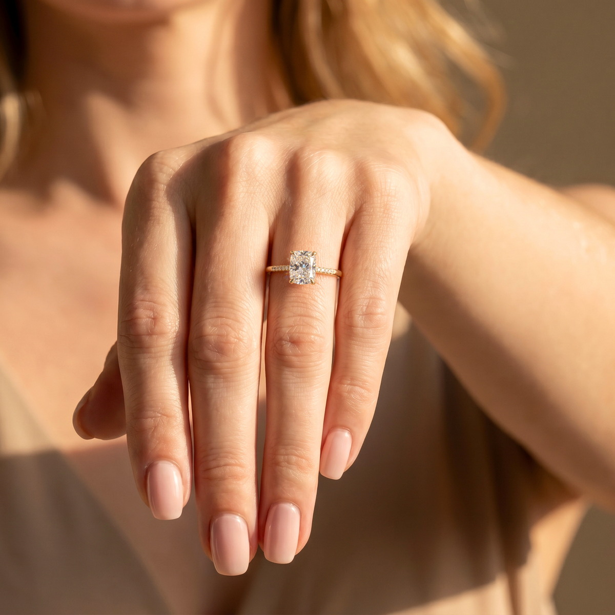 A woman wearing a yellow gold cushion cut moissanite engagement ring with a pavé diamond band on her ring finger.