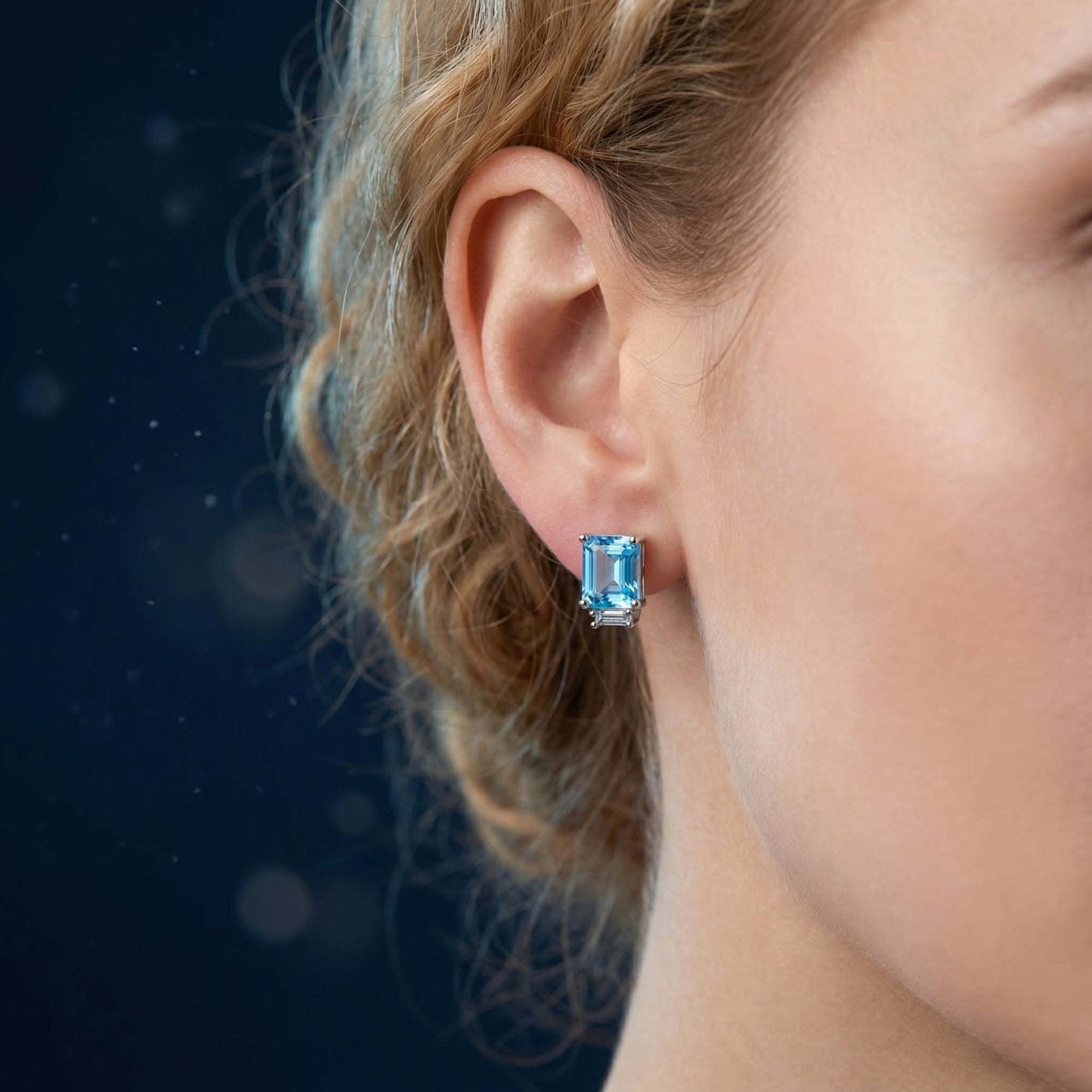 Emerald cut blue topaz earring in white gold worn on a woman's ear, demonstrating size and brilliance.