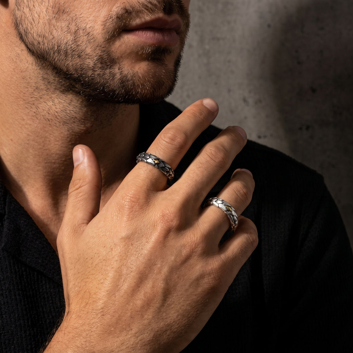 Man wearing two dragon-scale open rings with gold-colored accents on adjacent fingers near his neck.