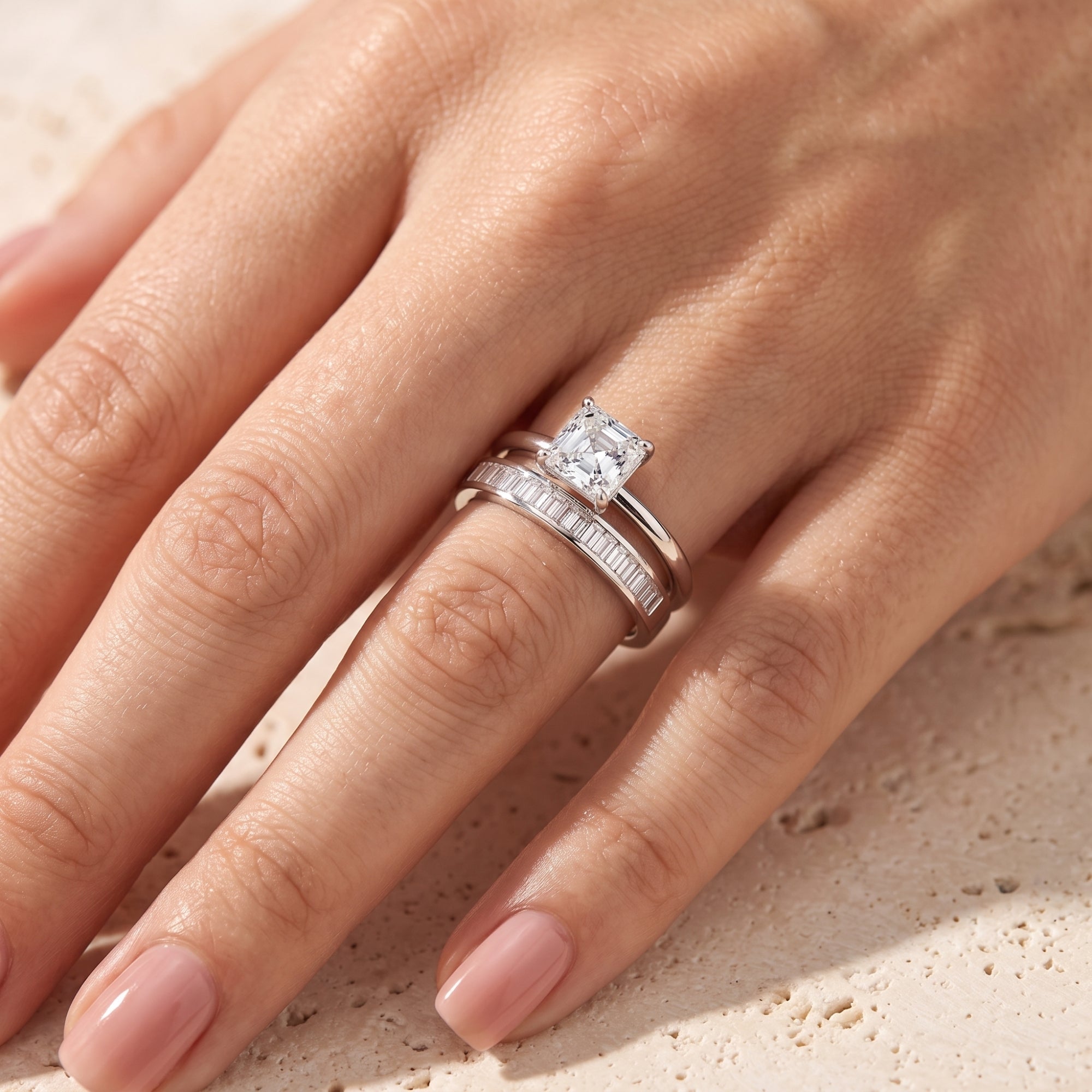 Square-cut simulated diamond solitaire and baguette eternity band in silver worn on a woman's ring finger.