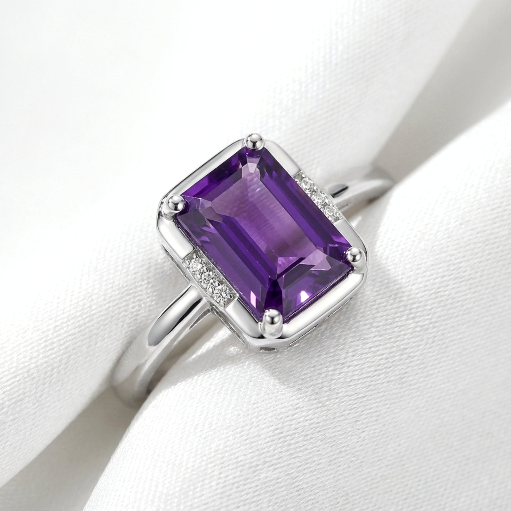 Macro view of an emerald cut purple amethyst and side stone accents in a sterling silver solitaire ring.