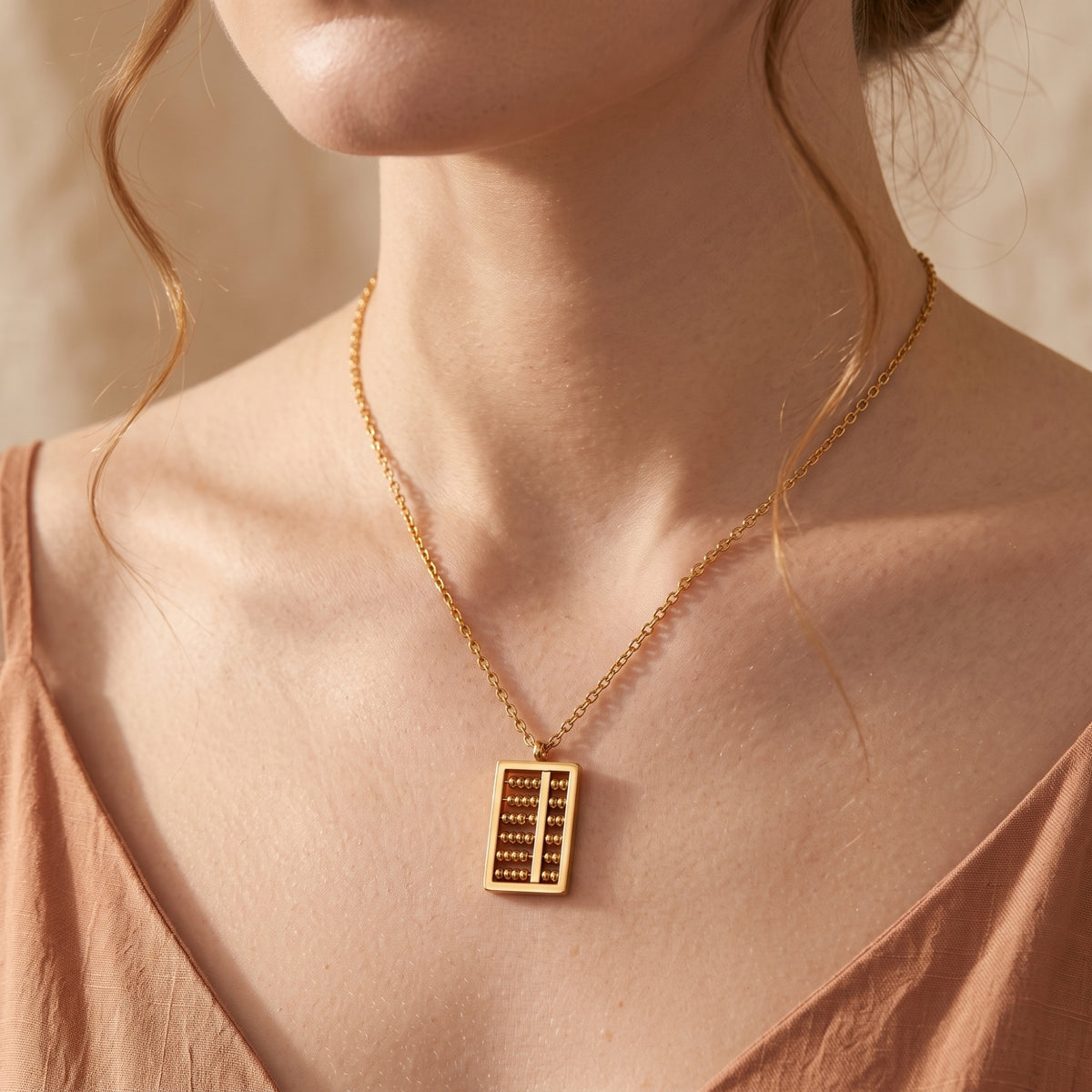 Close-up of a model wearing the gold-tone abacus pendant on a thin link chain over a terracotta top.