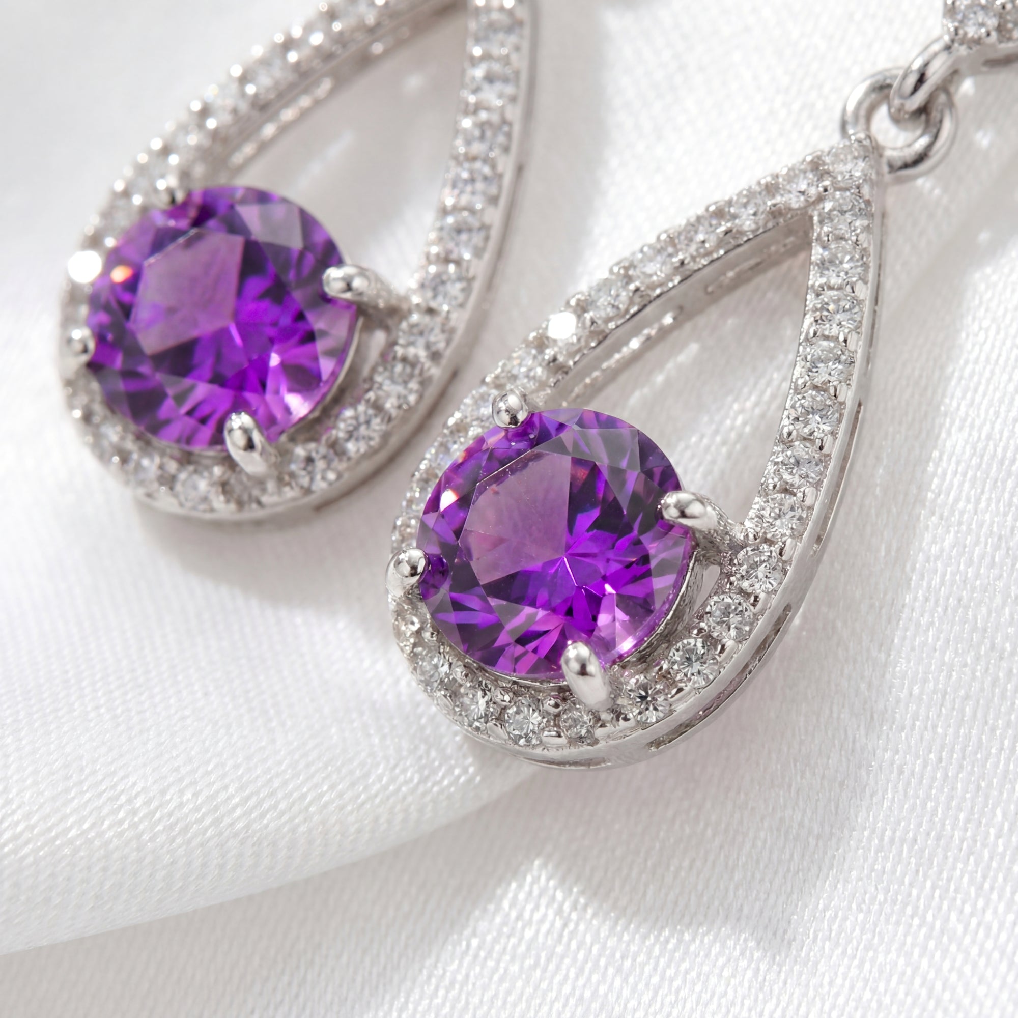 Macro view of round-cut simulated amethyst stones in sterling silver pave teardrop settings.