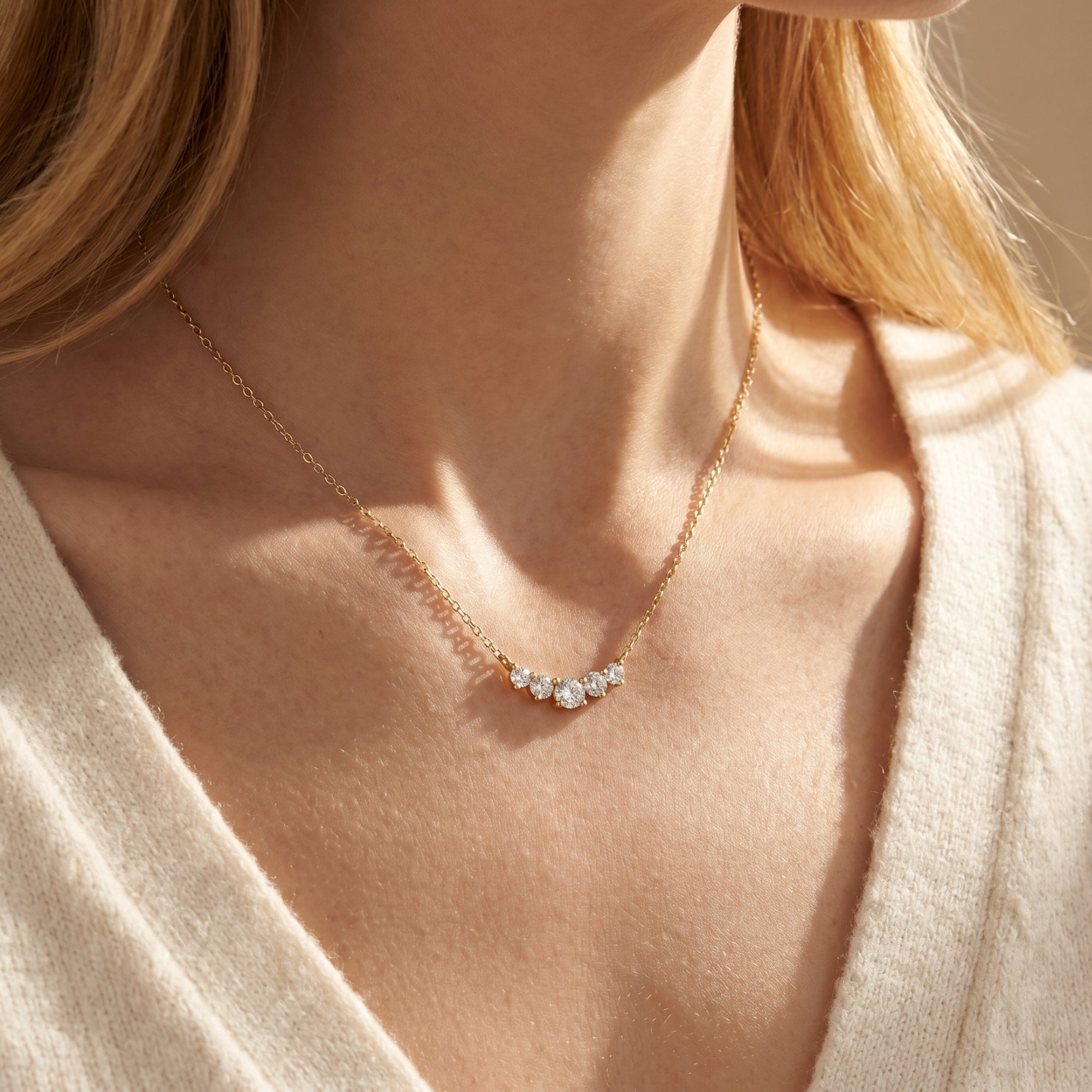 Woman wearing the Antonella yellow gold moissanite arc necklace over a cream knit sweater.