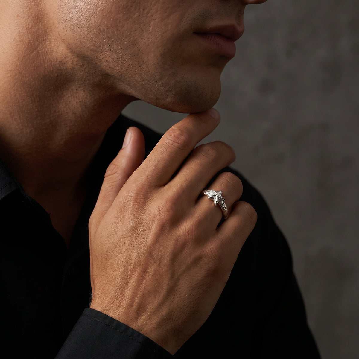 Man wearing a textured silver star ring on his finger with his hand resting at his chin.