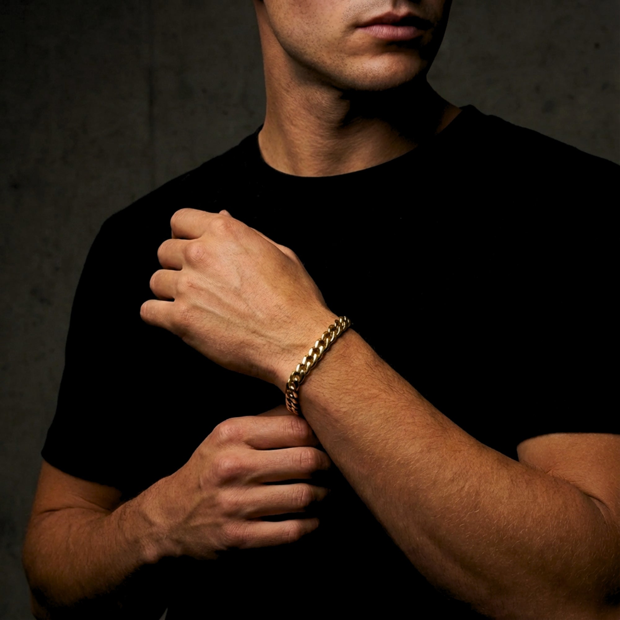 Close-up of a man's wrist wearing a gold stainless steel Cuban link bracelet against a dark background.